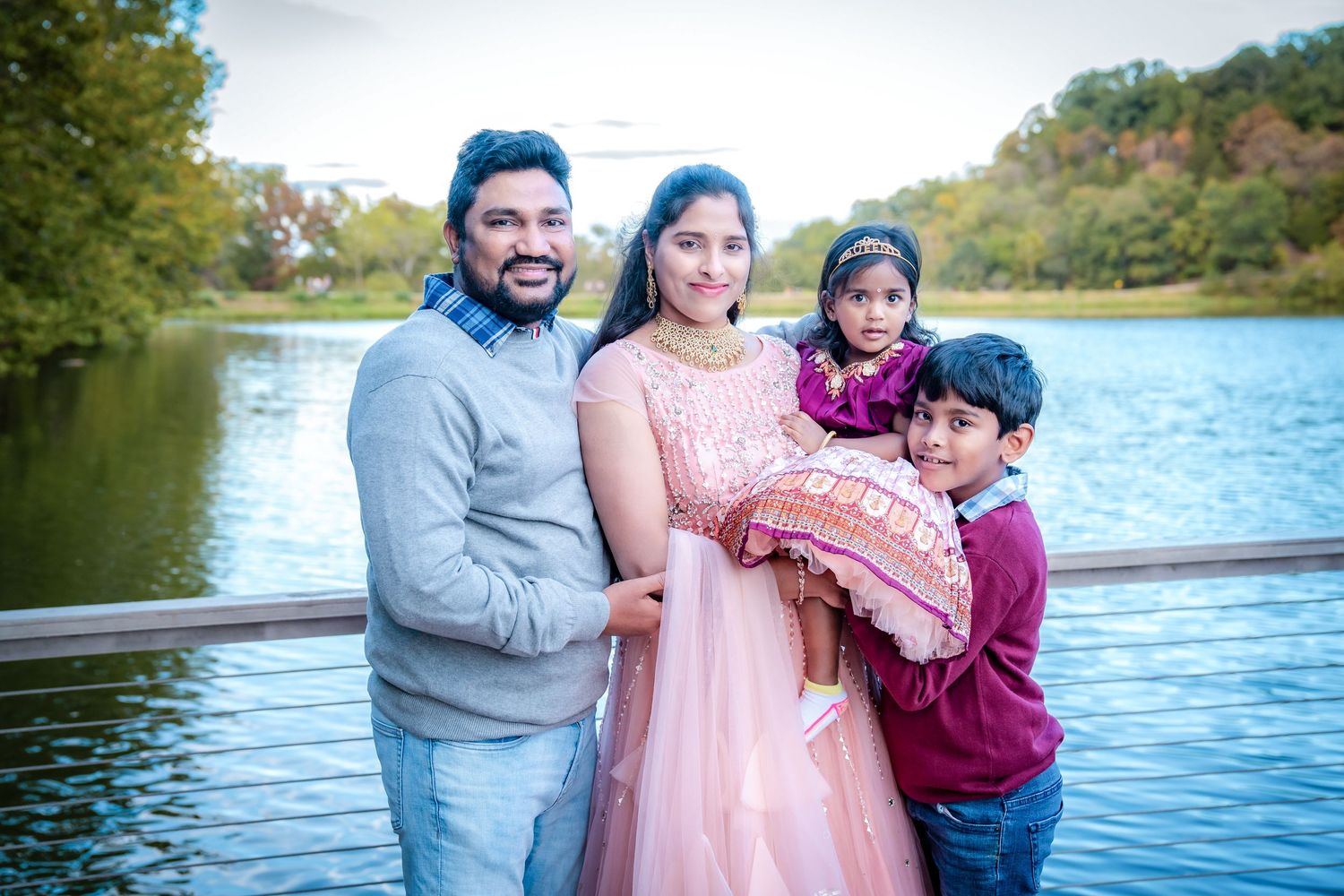 Family wearing pink and blue outfits smiles together near a waterfront.