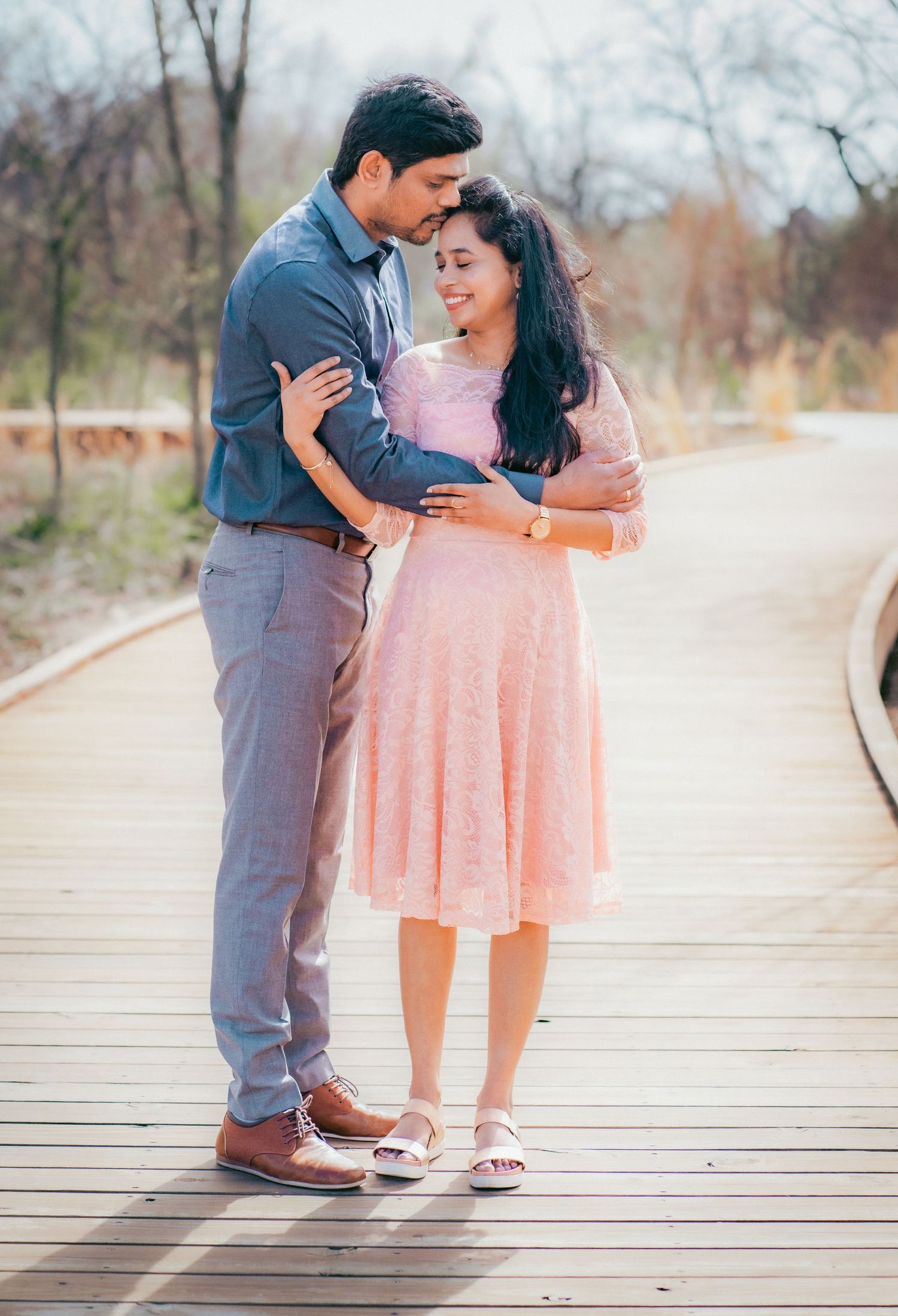 Romantic couple poses on a wooden boardwalk in soft pastel tones.