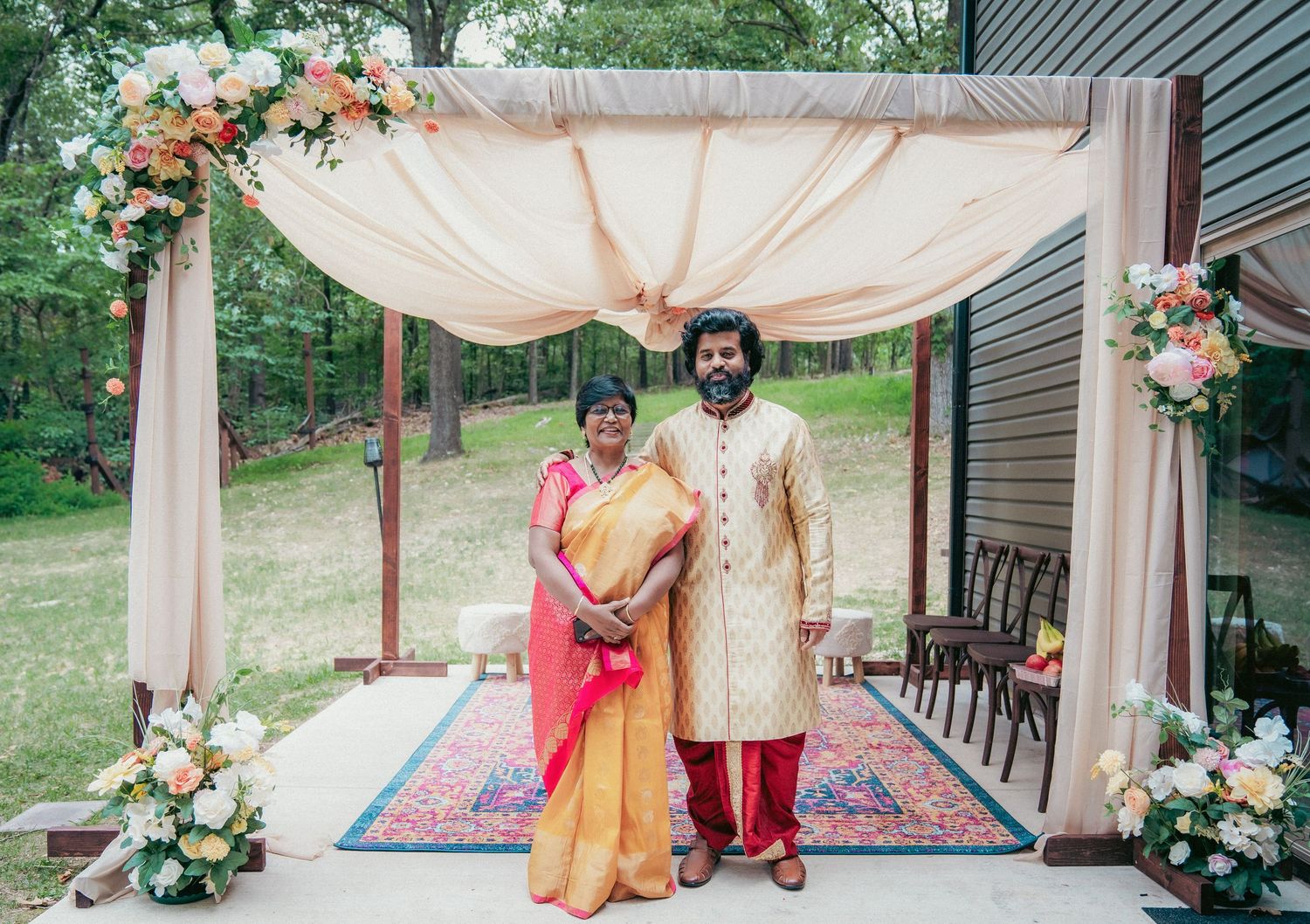 A wedding ceremony setup with peach drapes and oriental rugs on a patio surrounded by greenery.