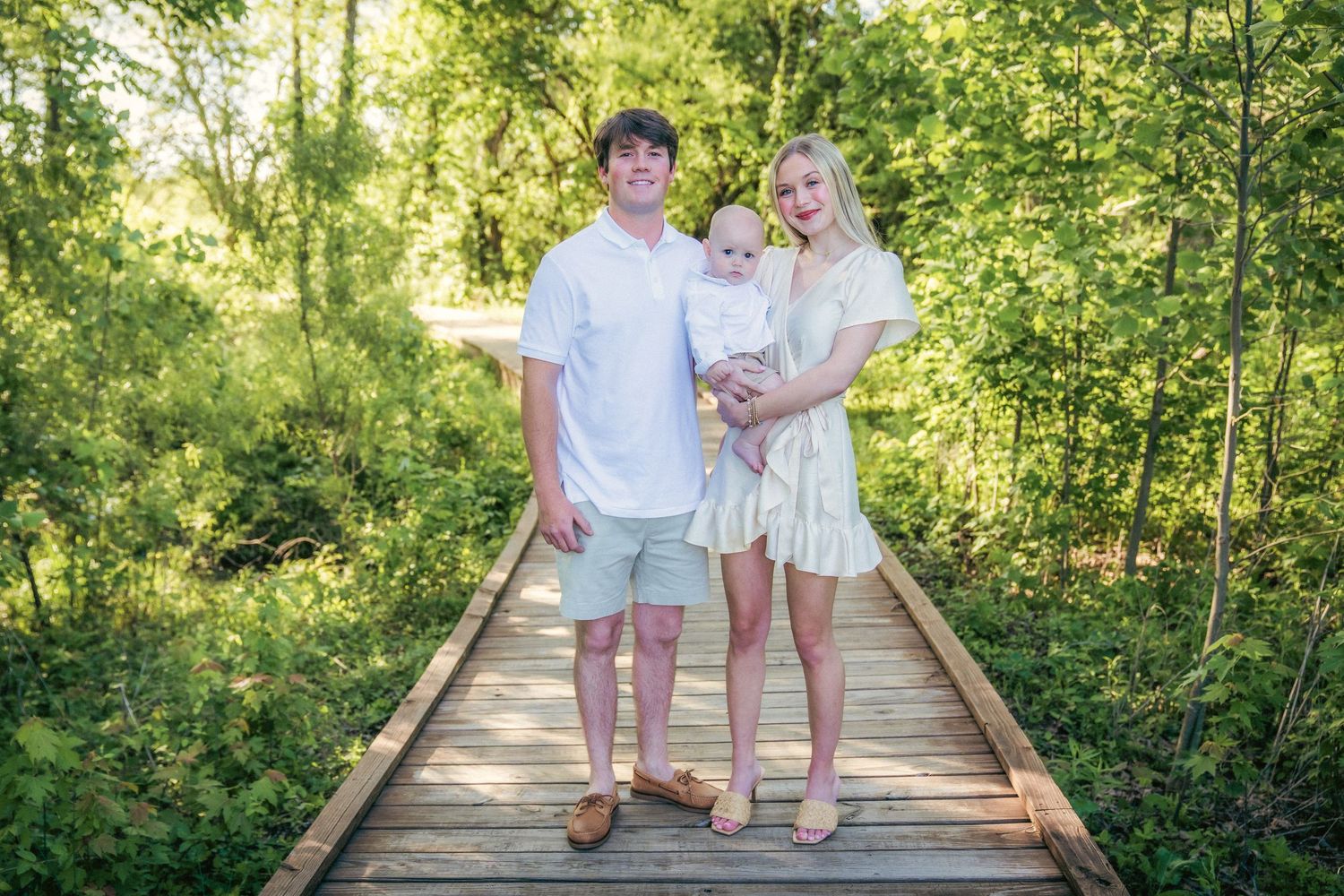 Family members walking together on wooden boardwalk surrounded by lush green foliage.