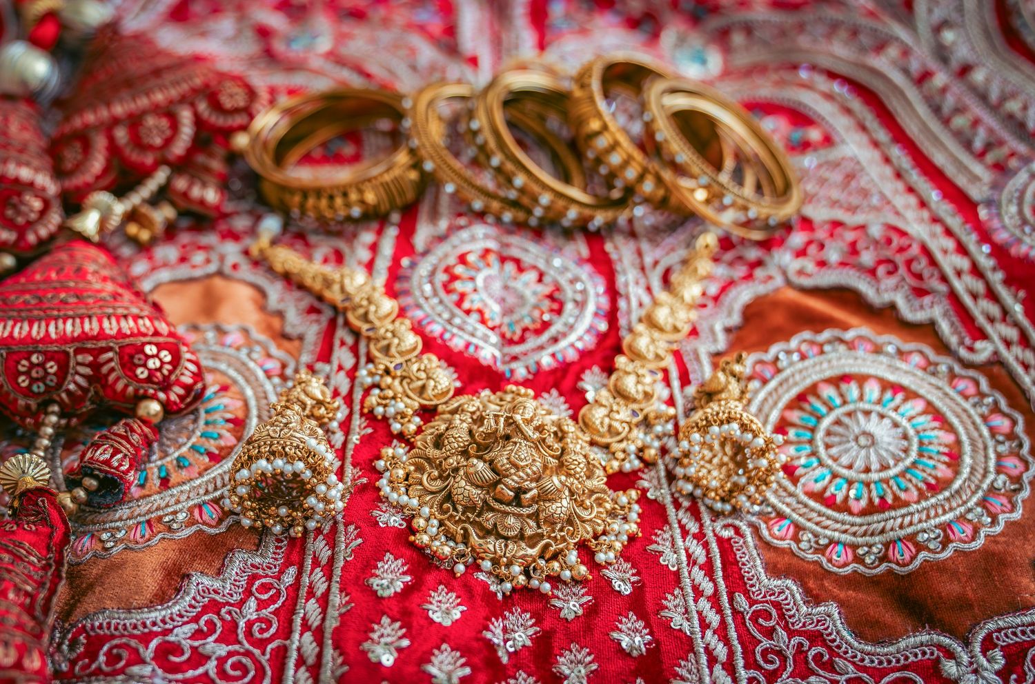 Traditional Indian wedding jewelry and bangles arranged on a red embroidered fabric.