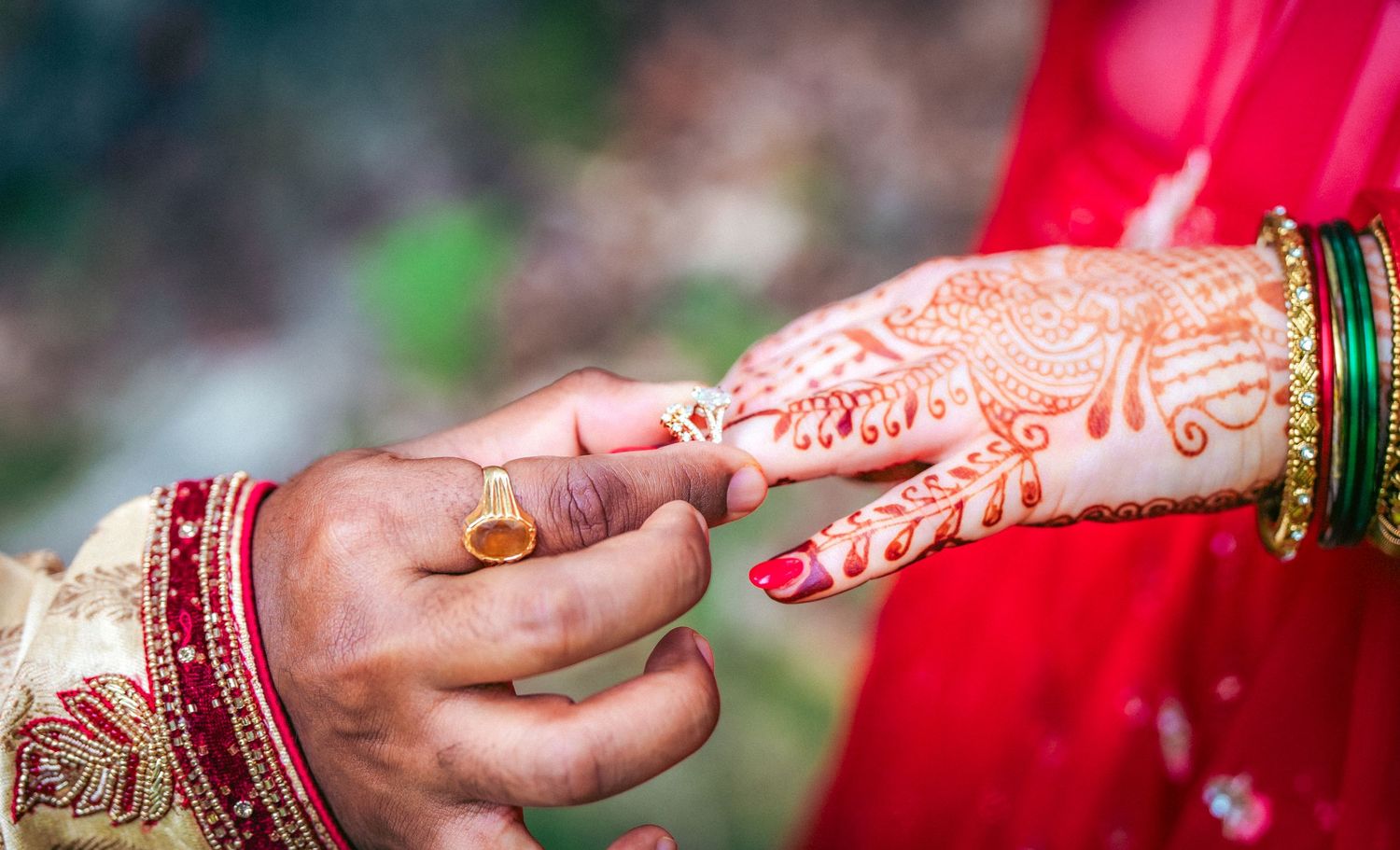 Close-up of decorated hands during Indian wedding ceremony against red background.