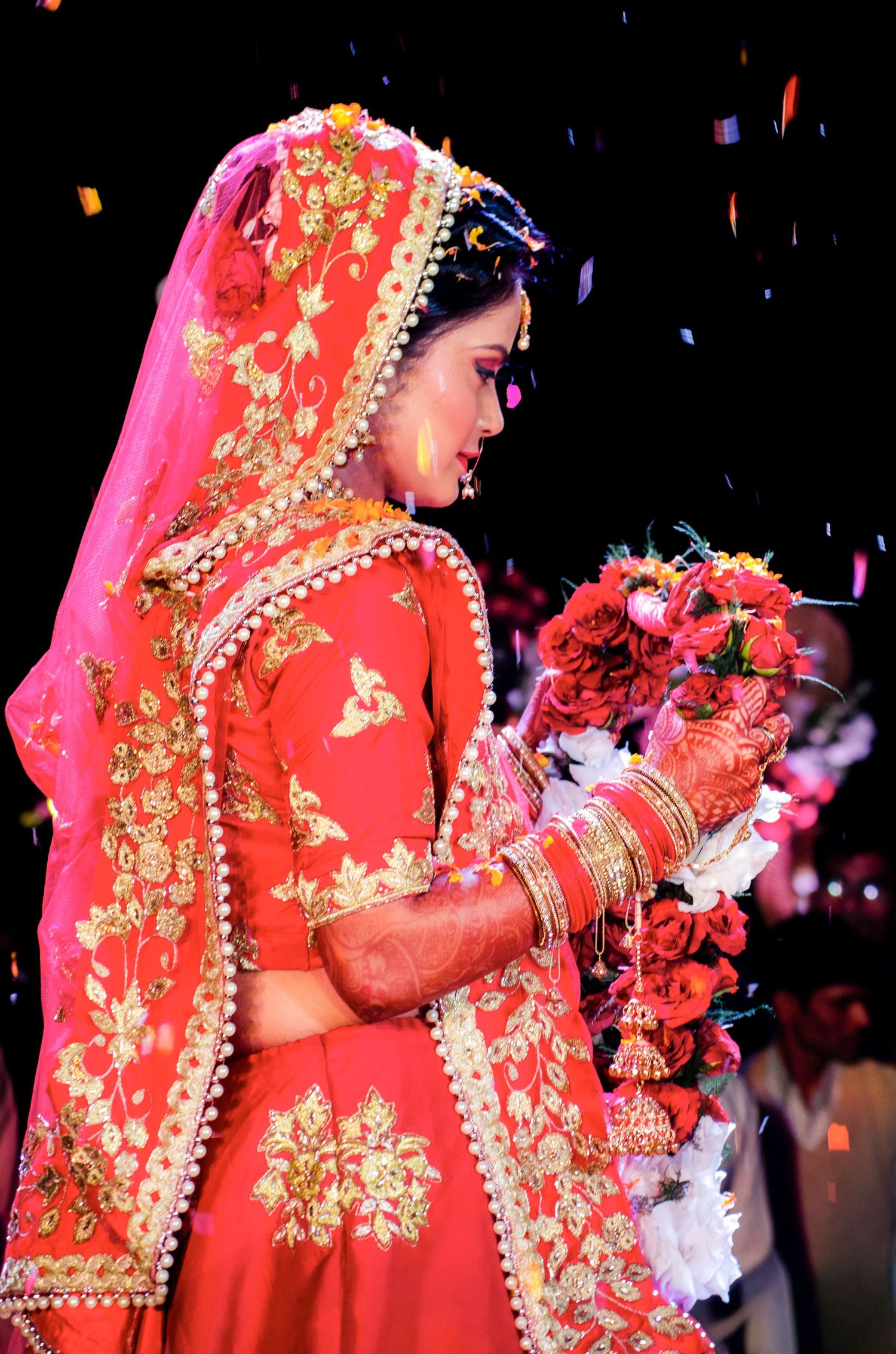 Traditional Indian bride in a vibrant red and gold embroidered lehenga holding a decorative bouquet.