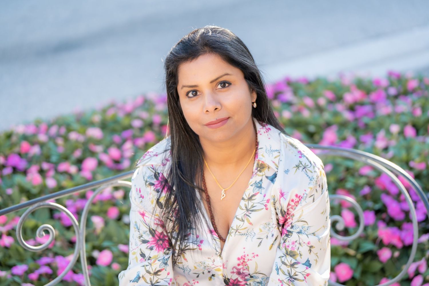 Person in floral dress poses in colorful flower garden with purple and pink blooms.