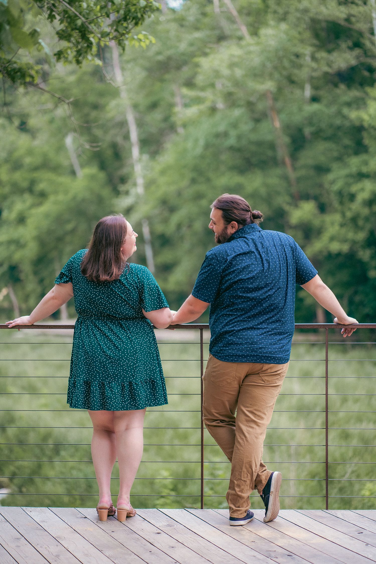 A couple leans on a railing overlooking scenic greenery during their engagement photos.