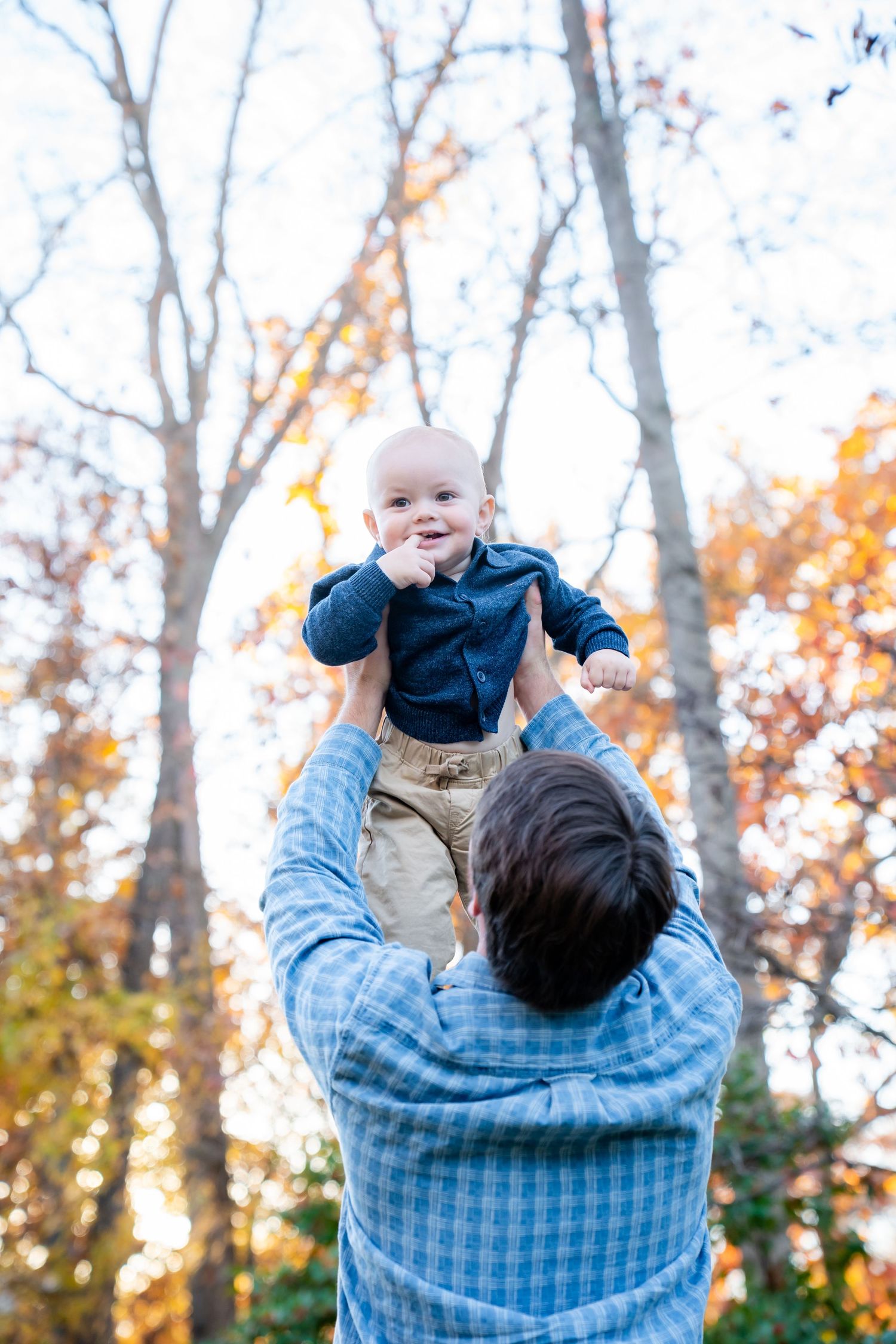Playful moment captured in autumn woods with baby being lifted high in the air.