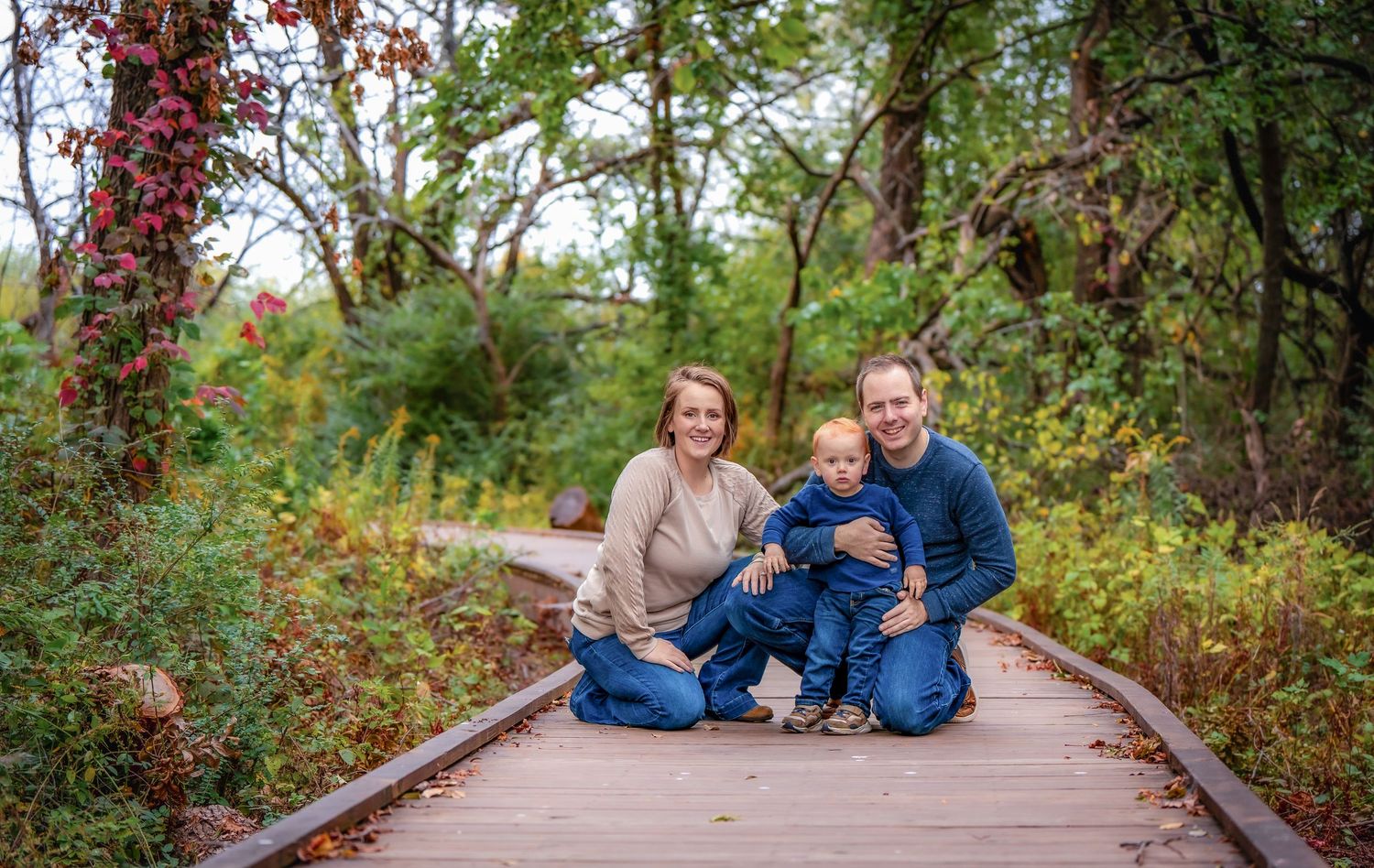 A family sitting together on a wooden boardwalk surrounded by fall foliage and red berries.