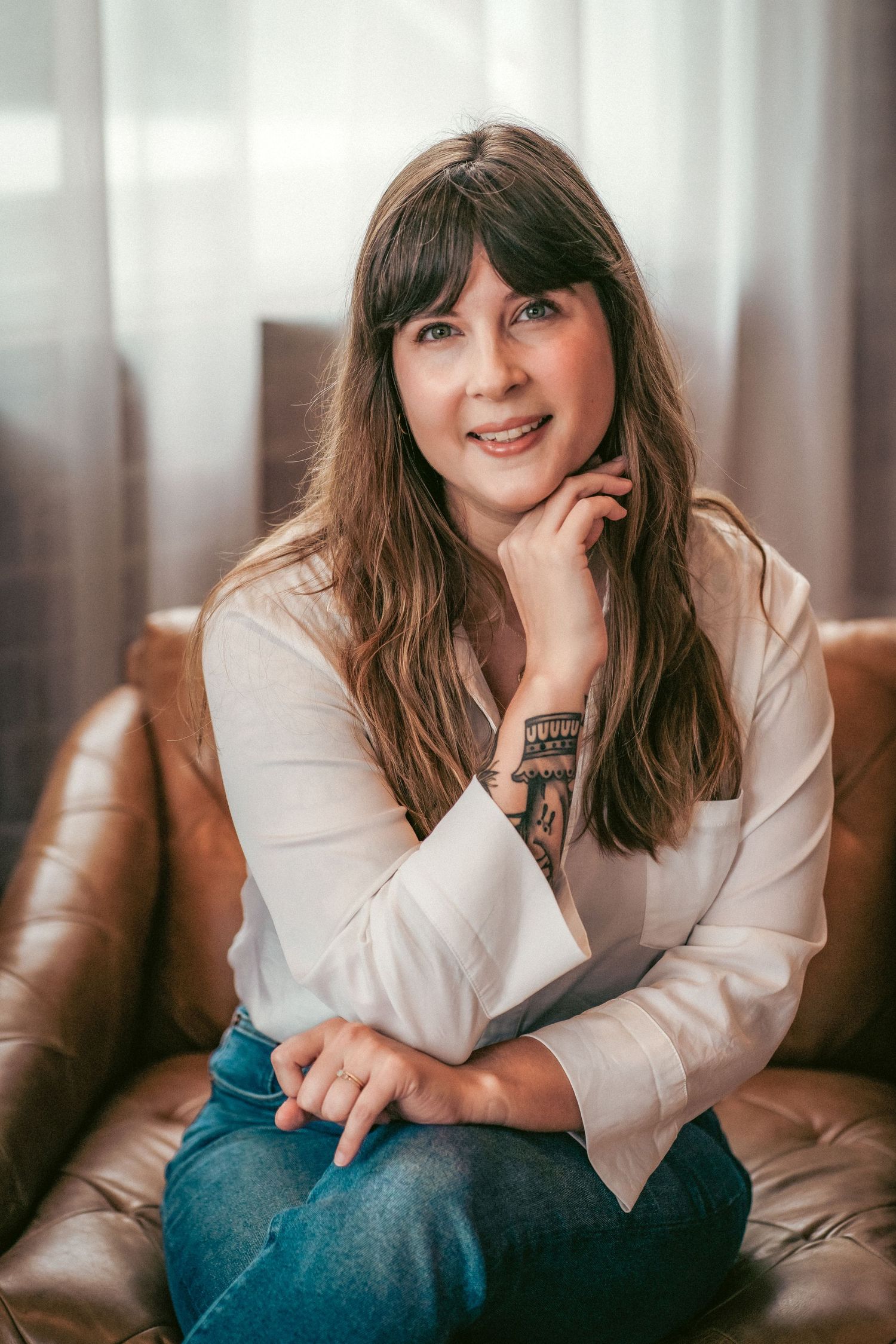 A person in a white shirt and jeans relaxes on a brown leather couch.