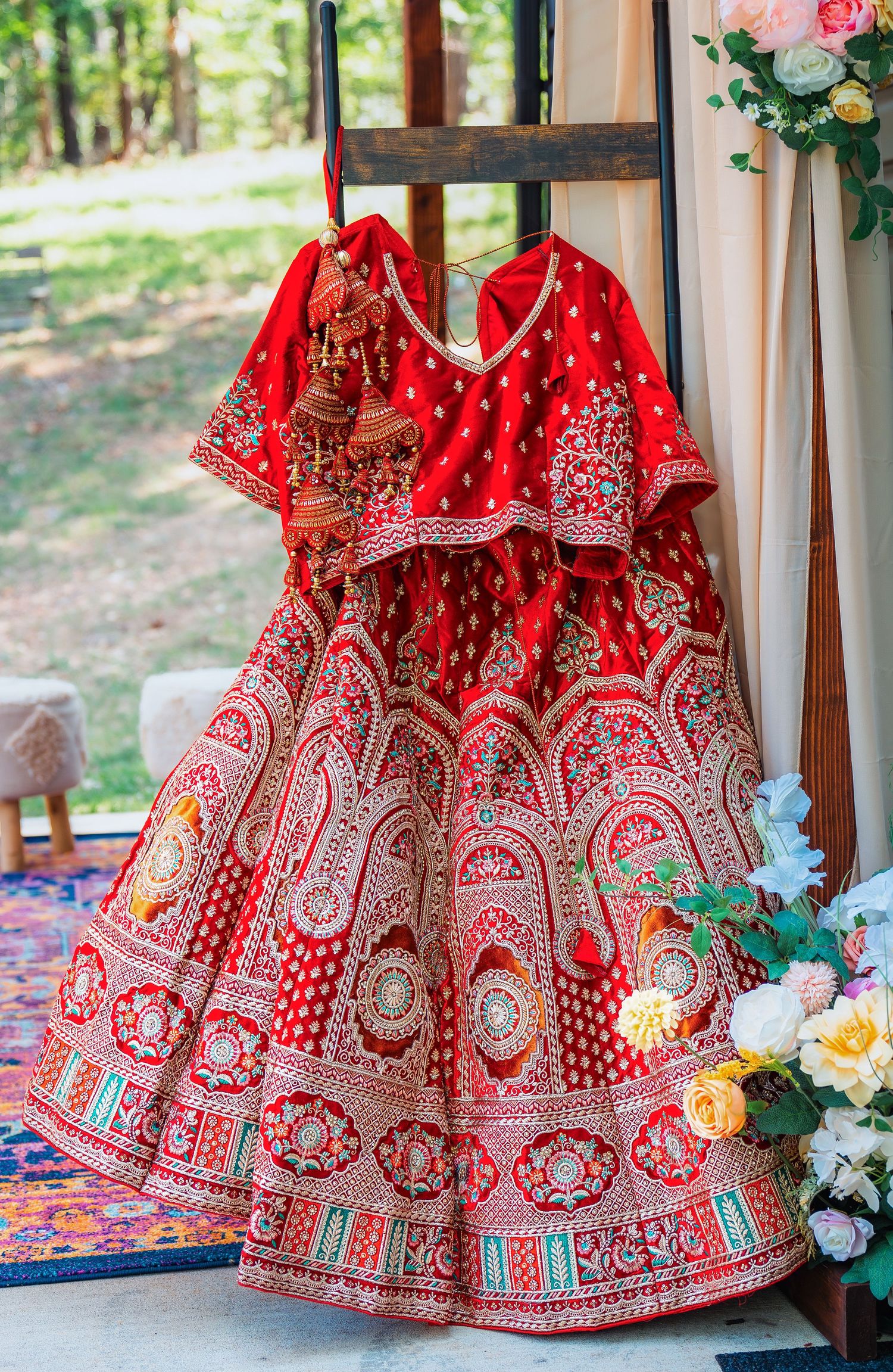 A traditional red Indian bridal lehenga with intricate embroidery displayed on a wooden ladder.