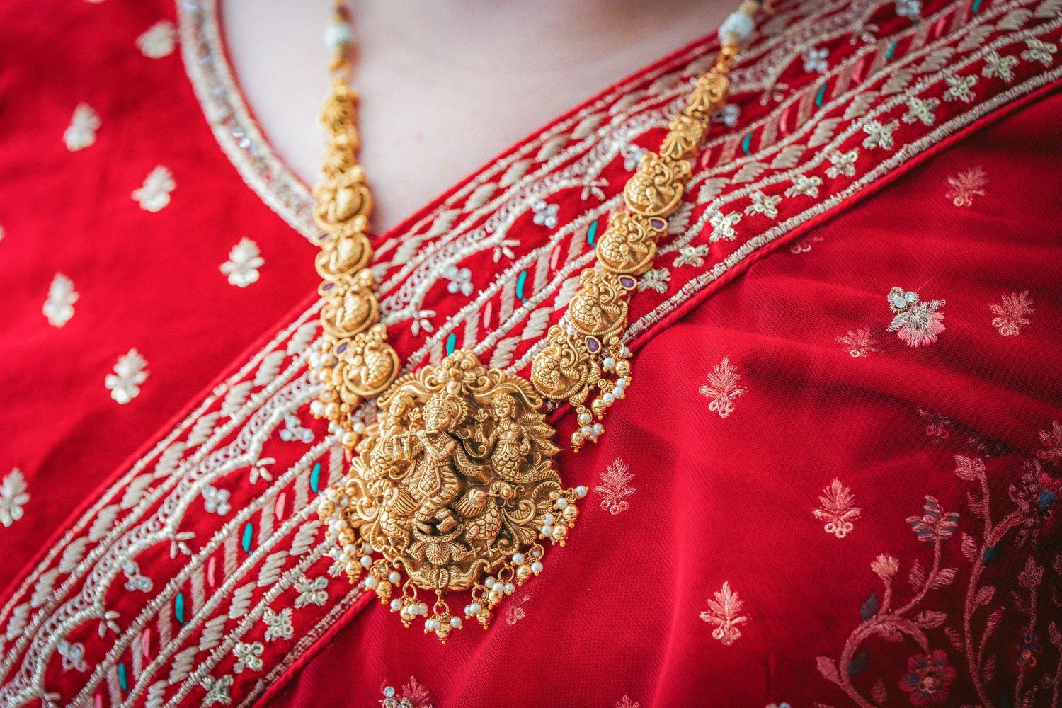 Ornate gold necklace and embroidery details on red Indian bridal wear.