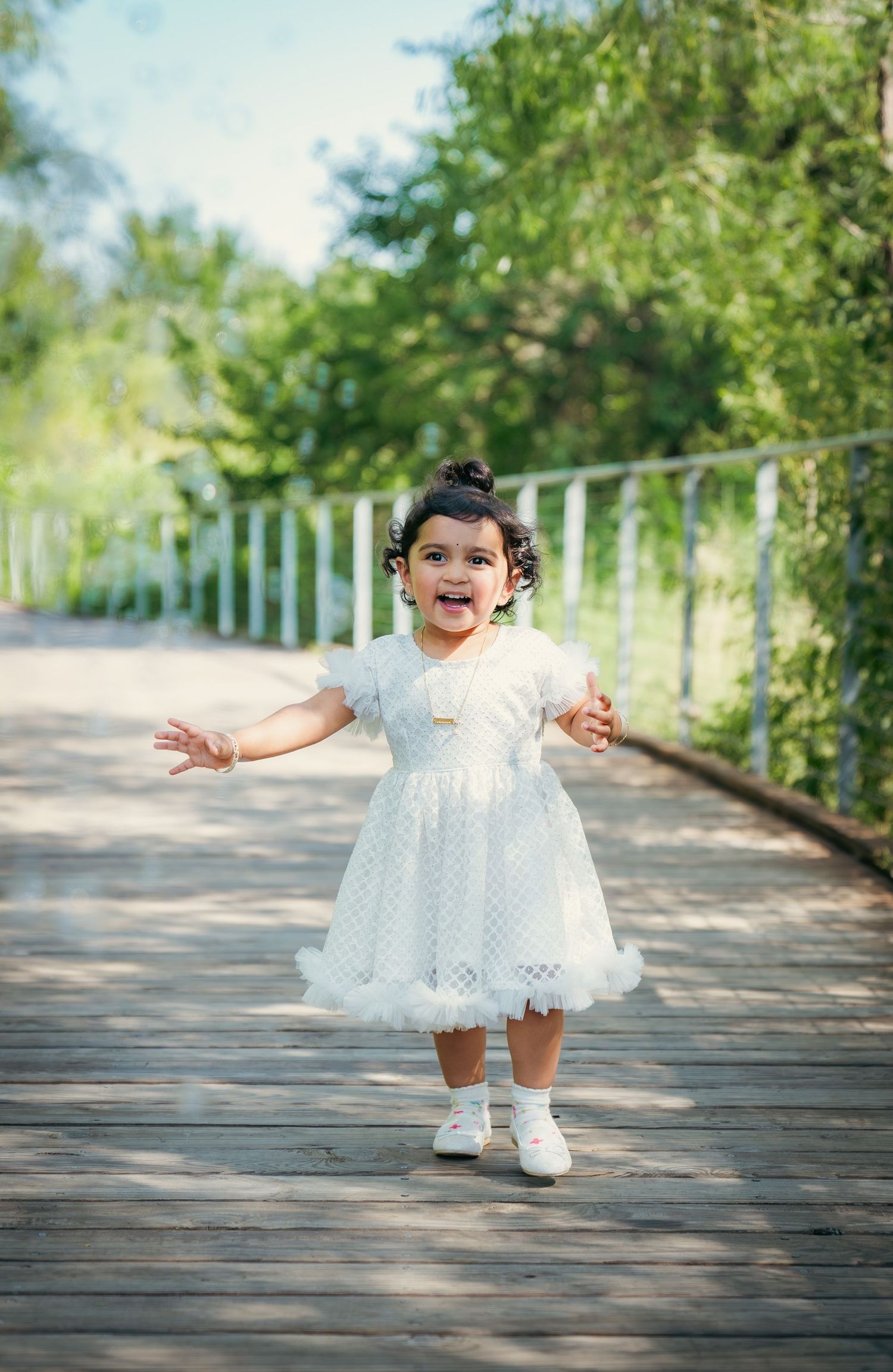 Small child in white dress twirling and playing on wooden boardwalk.