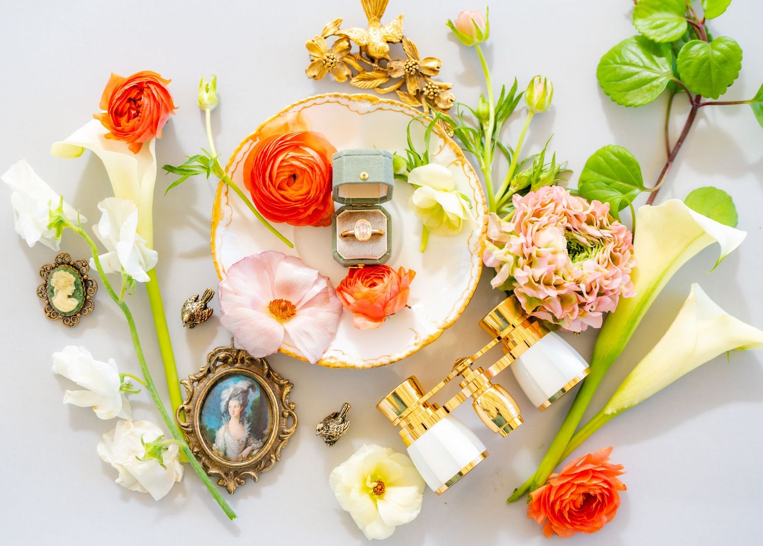Wedding styling details with orange ranunculus flowers and vintage accessories on light background.