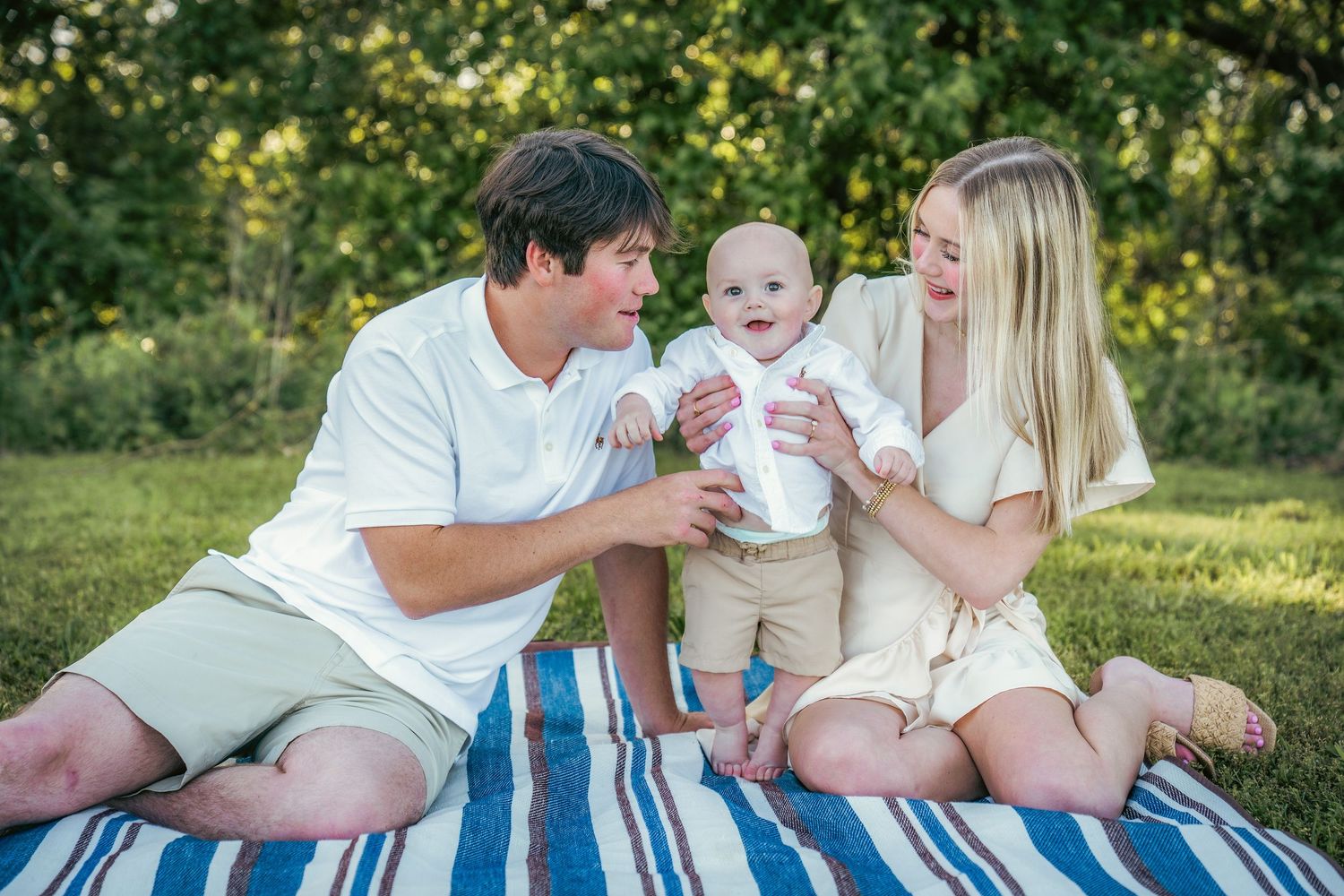 Family relaxes on striped blanket during outdoor photo session.