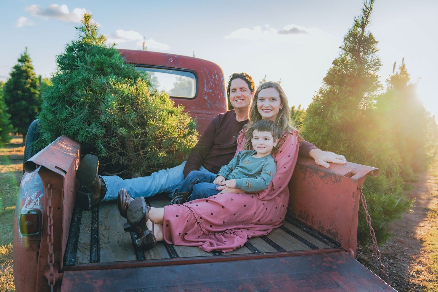 Family relaxing together on vintage red truck bed during sunset at Christmas tree farm.