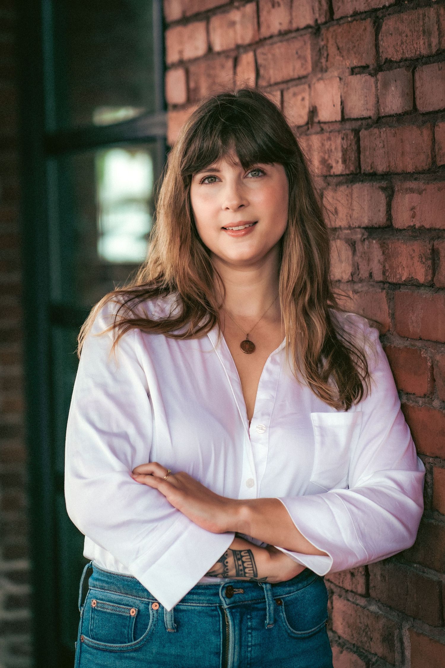 A person in a white button-down shirt poses against a rustic brick wall.