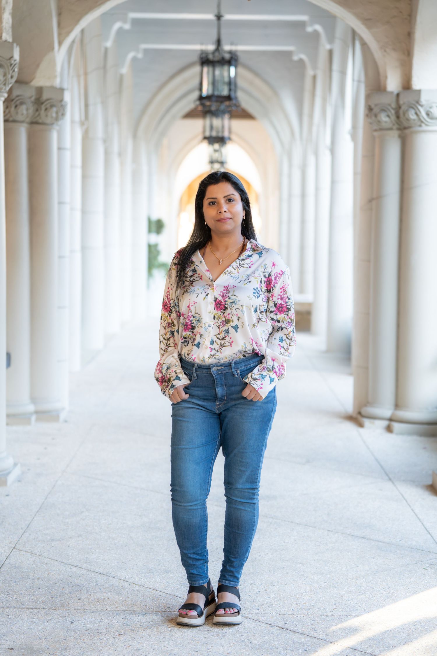 A person in a floral top and jeans poses in a series of photos along an elegant white columned corridor.