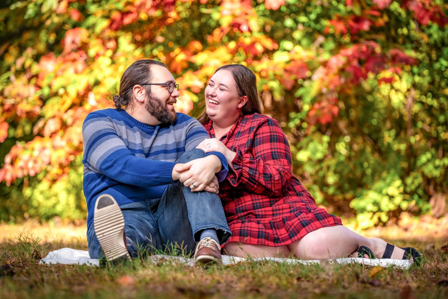 A couple shares intimate moments on a blanket surrounded by vibrant fall foliage.