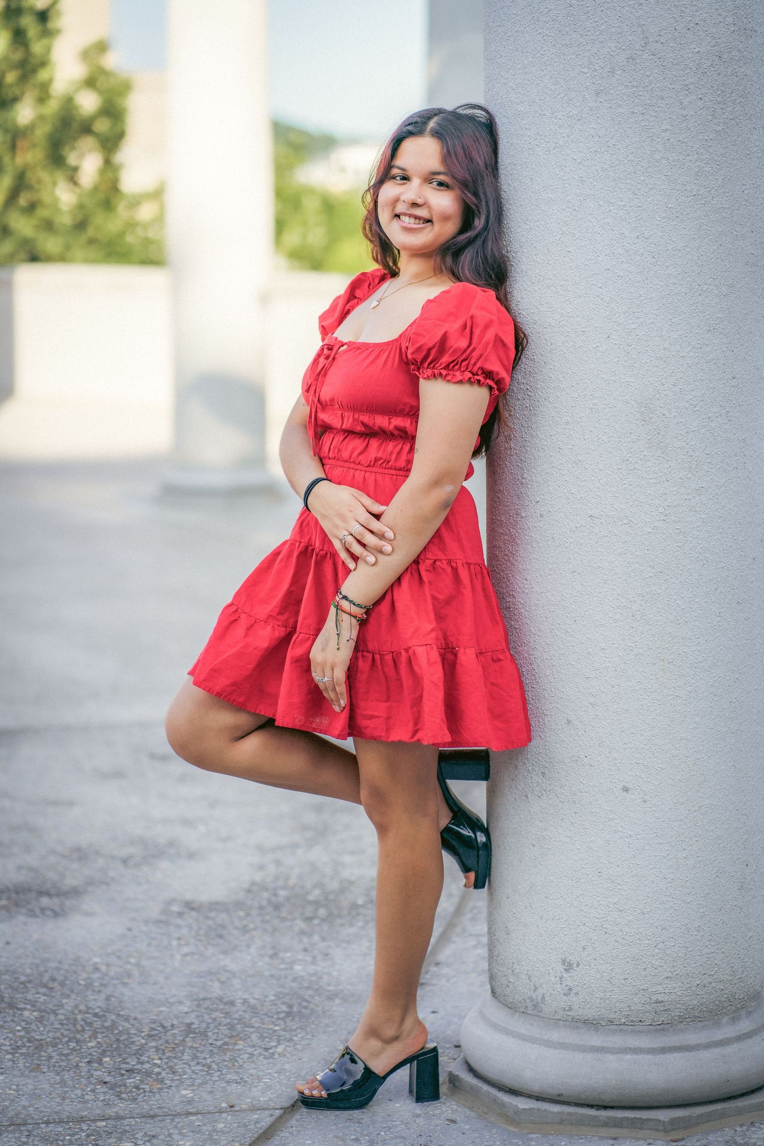 Playful pose in red dress against white architectural column for a senior shoot.