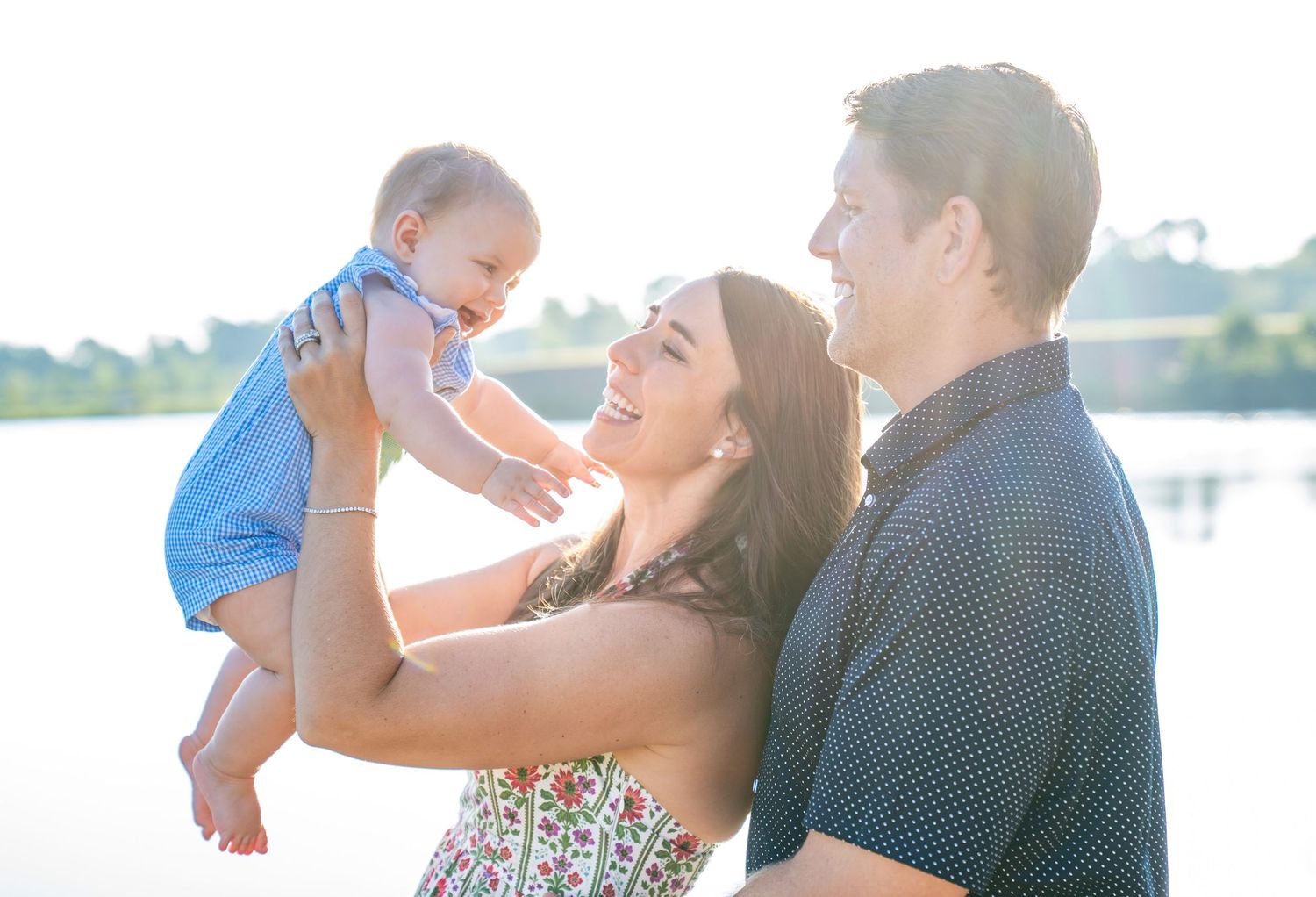 Family portrait at sunset by the water with joyful expressions and casual summer outfits.