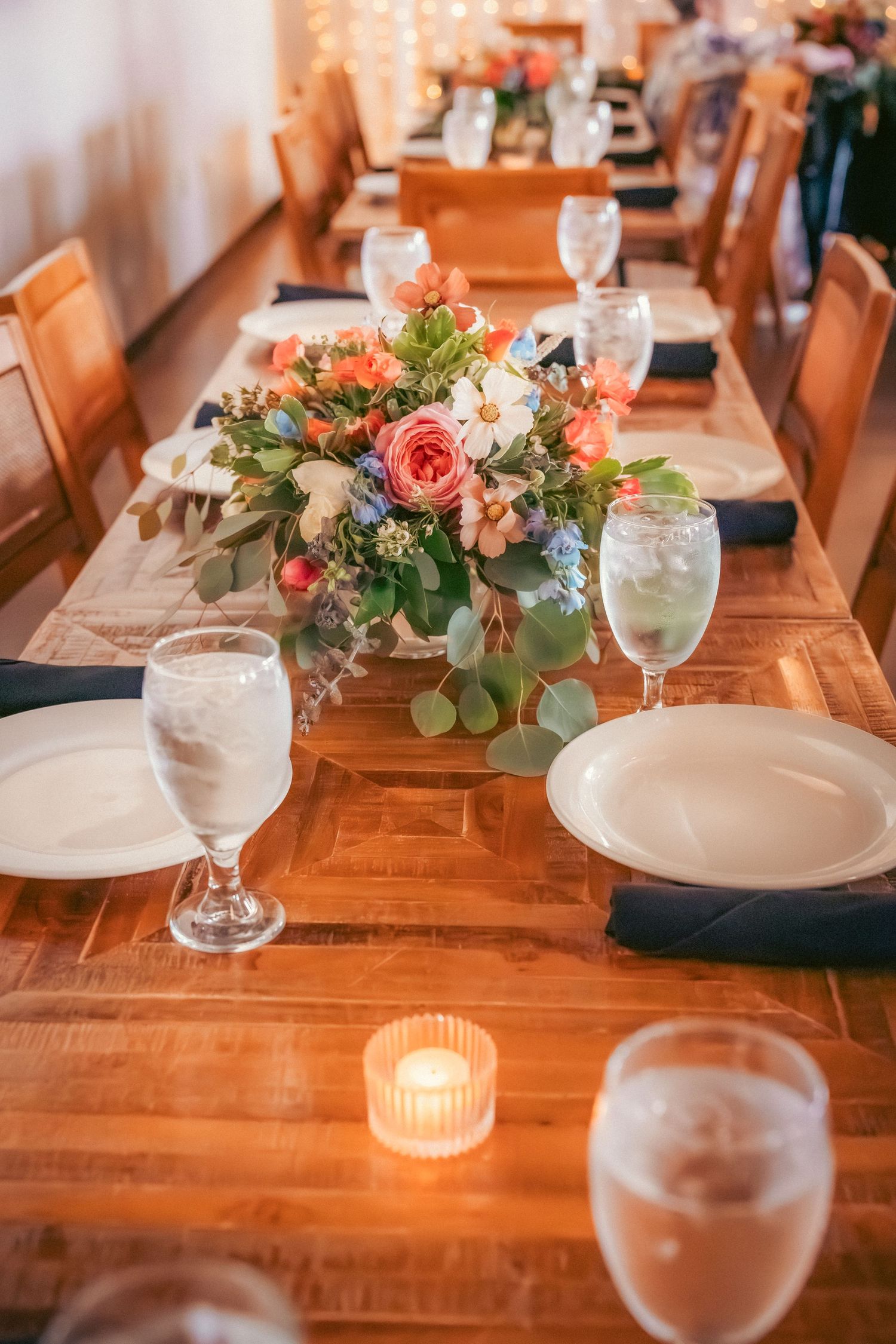 Rustic wooden dining table set with floral centerpieces and glowing candle votives.