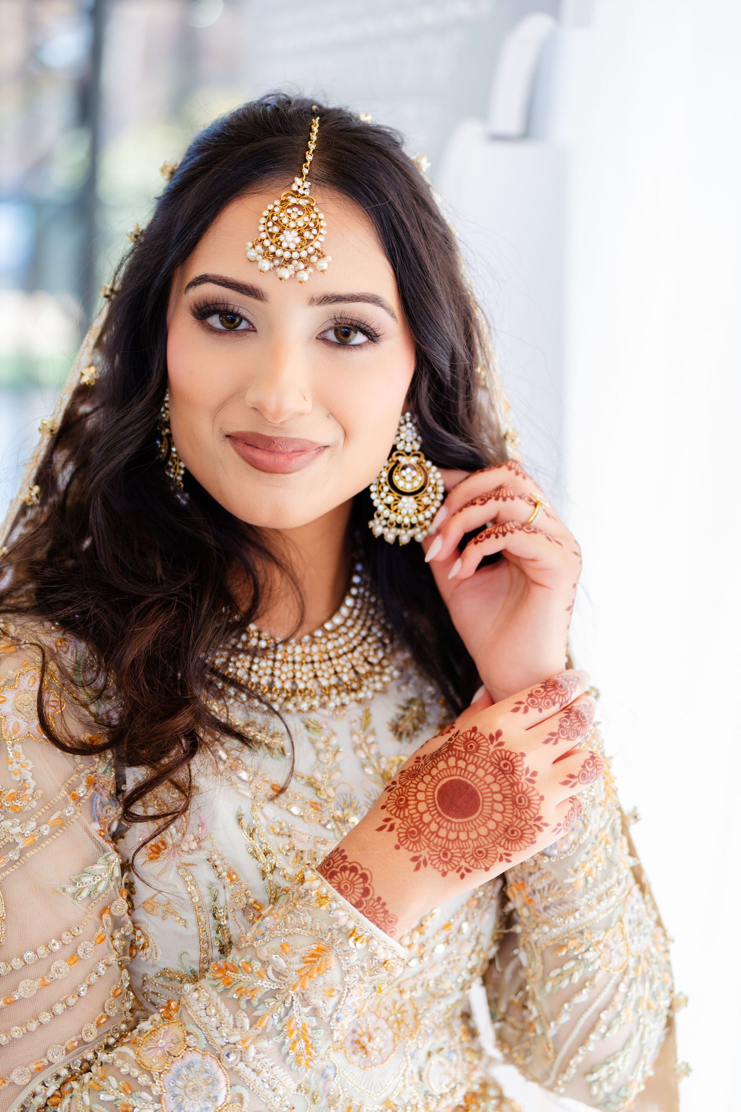 South Asian bride in embellished cream outfit with traditional jewelry and makeup.