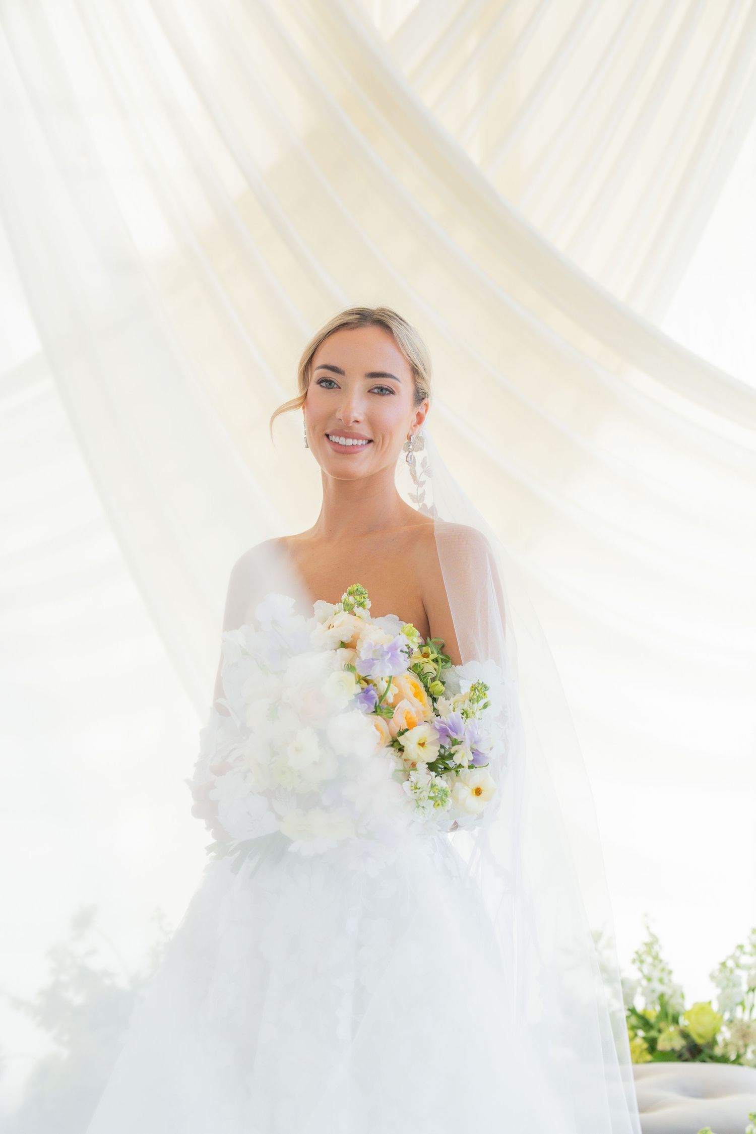Ethereal bridal portrait with soft lighting and spring bouquet against white draping.