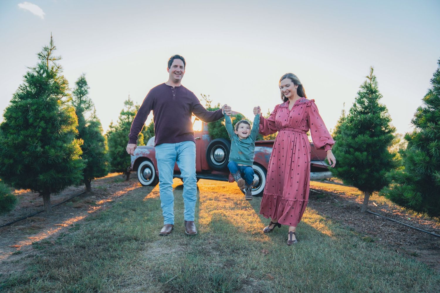 Family portrait session at sunset among evergreen trees with vintage red truck.