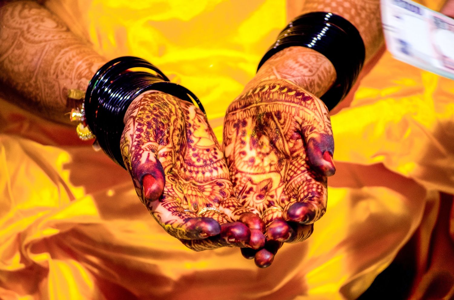 Close-up of hands decorated with intricate henna designs against warm golden lighting.