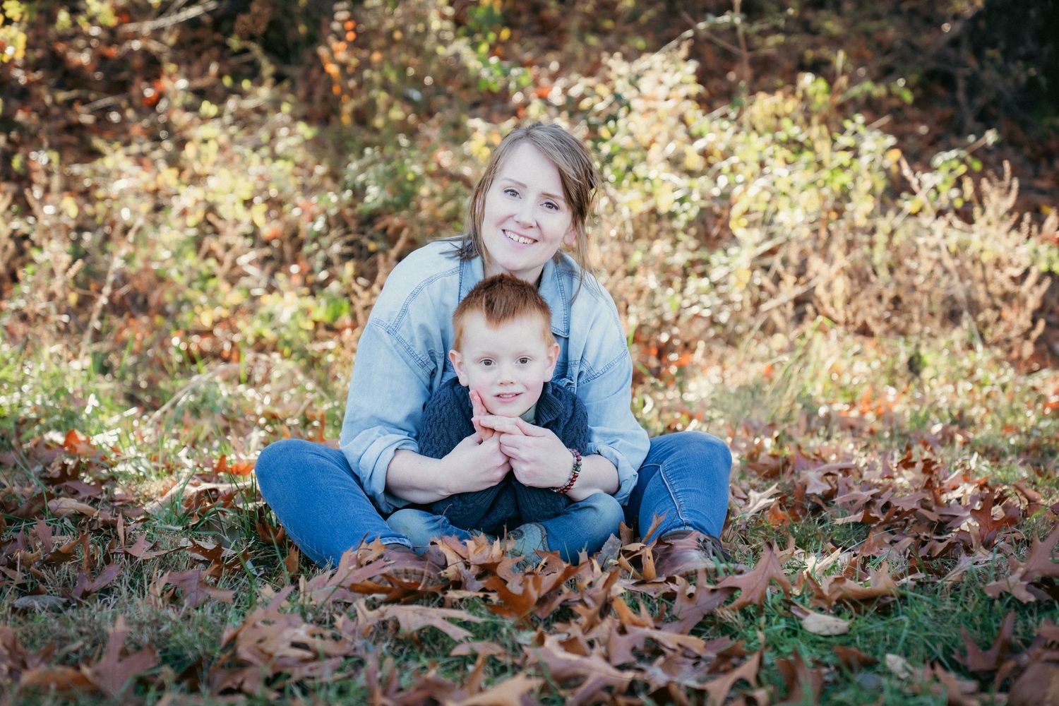 Family members lying on autumn leaves during outdoor photo session.