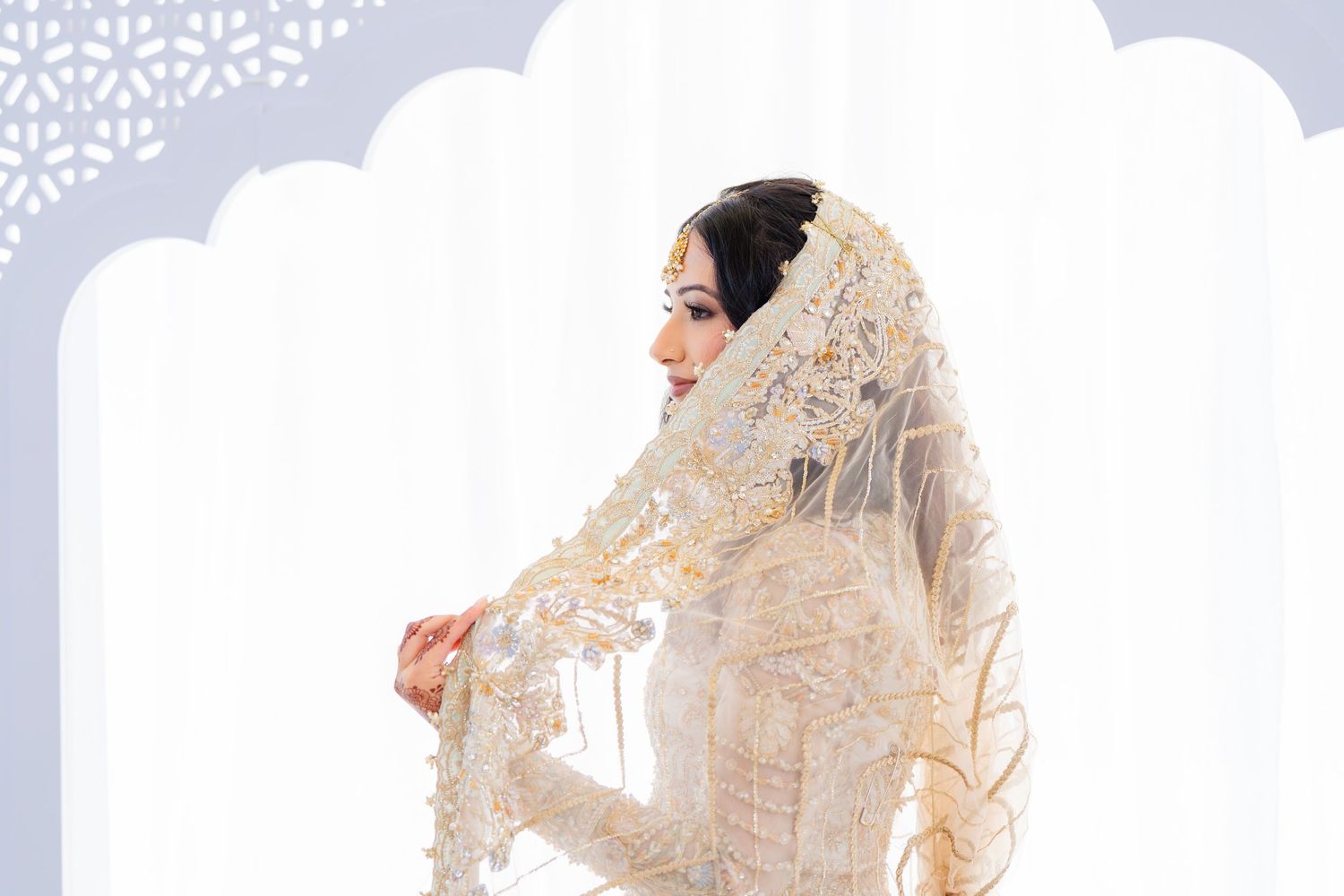 South Asian bride in cream lehenga with gold embellishments against white backdrop.