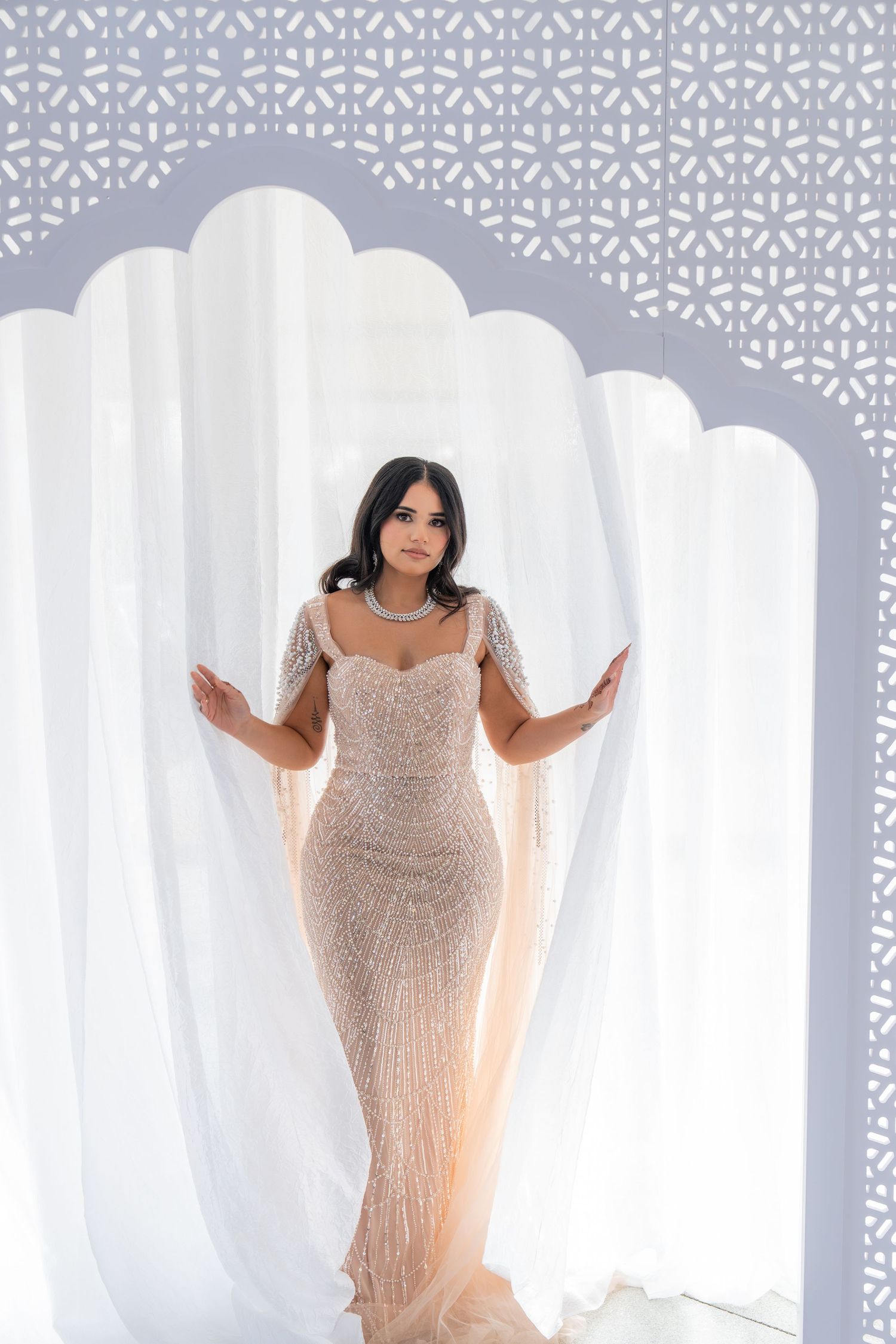 Elegant beaded champagne evening gown against white backdrop with ornate pattern details.