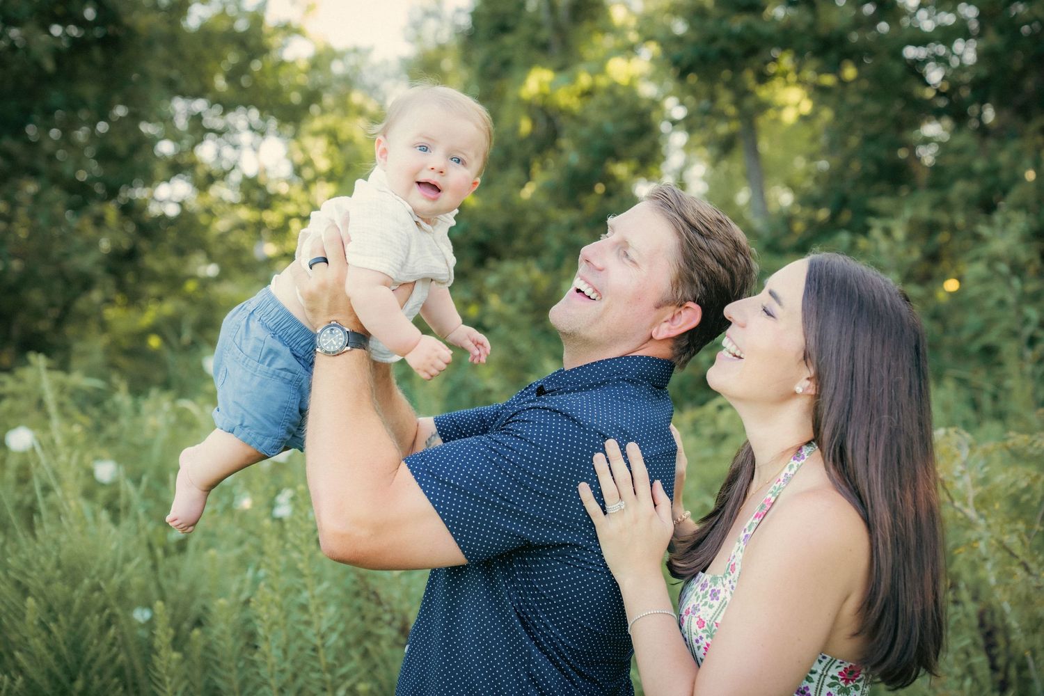 Joyful family moment outdoors with baby being lifted in the air.