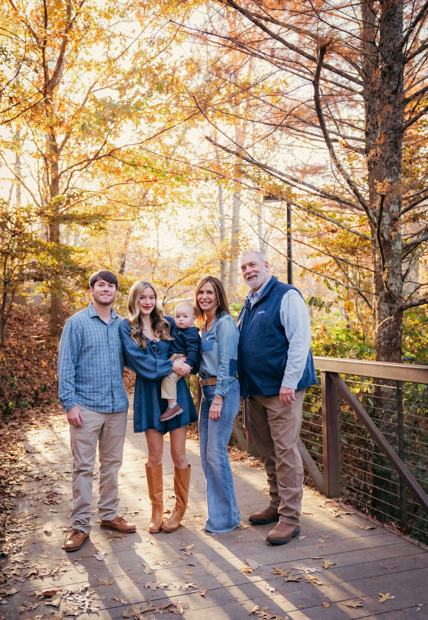 Family group posing on wooden deck during golden autumn sunset with fall foliage.
