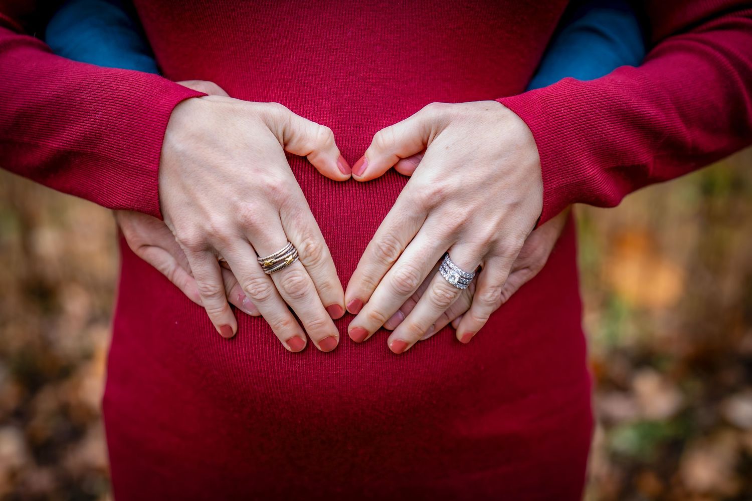 Close up of hands forming a heart shape against a burgundy dress.