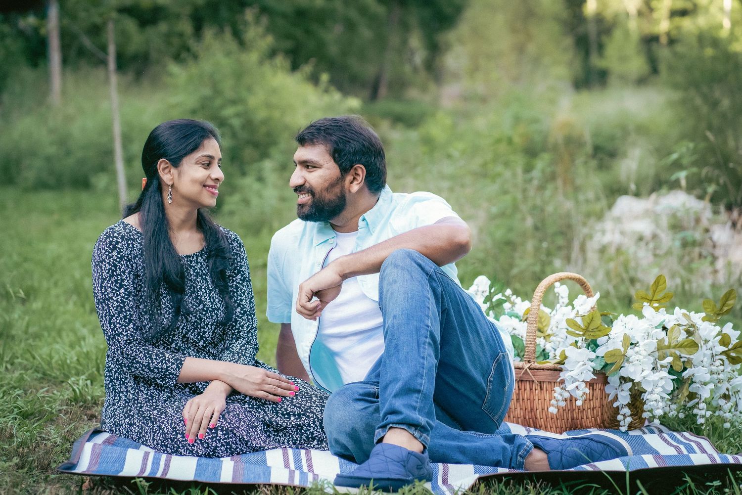 Couple enjoys a romantic picnic outdoors surrounded by greenery and flowers.