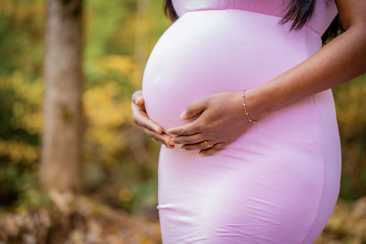 Close-up of hands cradling a baby bump in a pink maternity dress.
