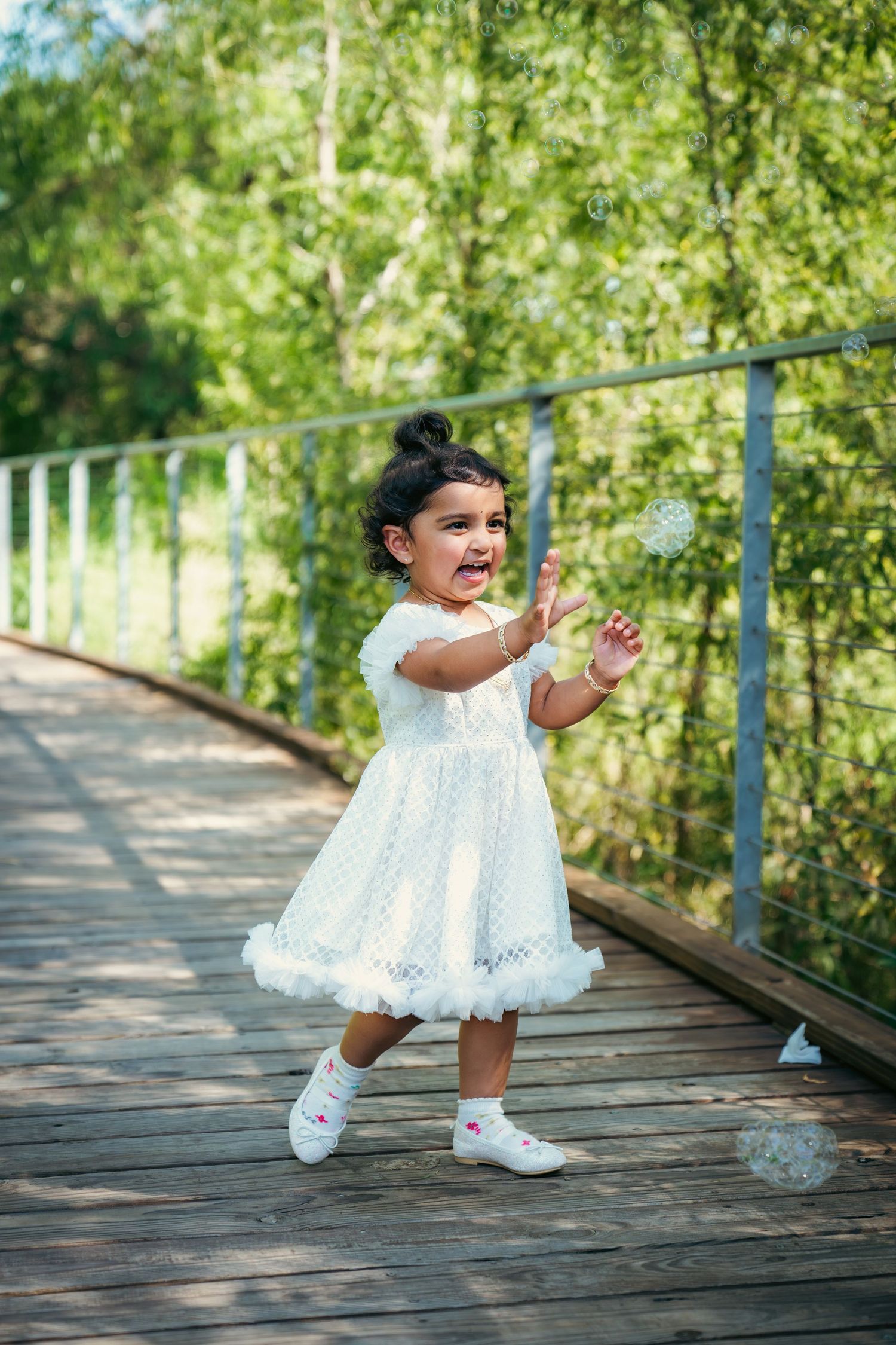 A small child in a white eyelet dress twirls and dances on an outdoor wooden walkway.