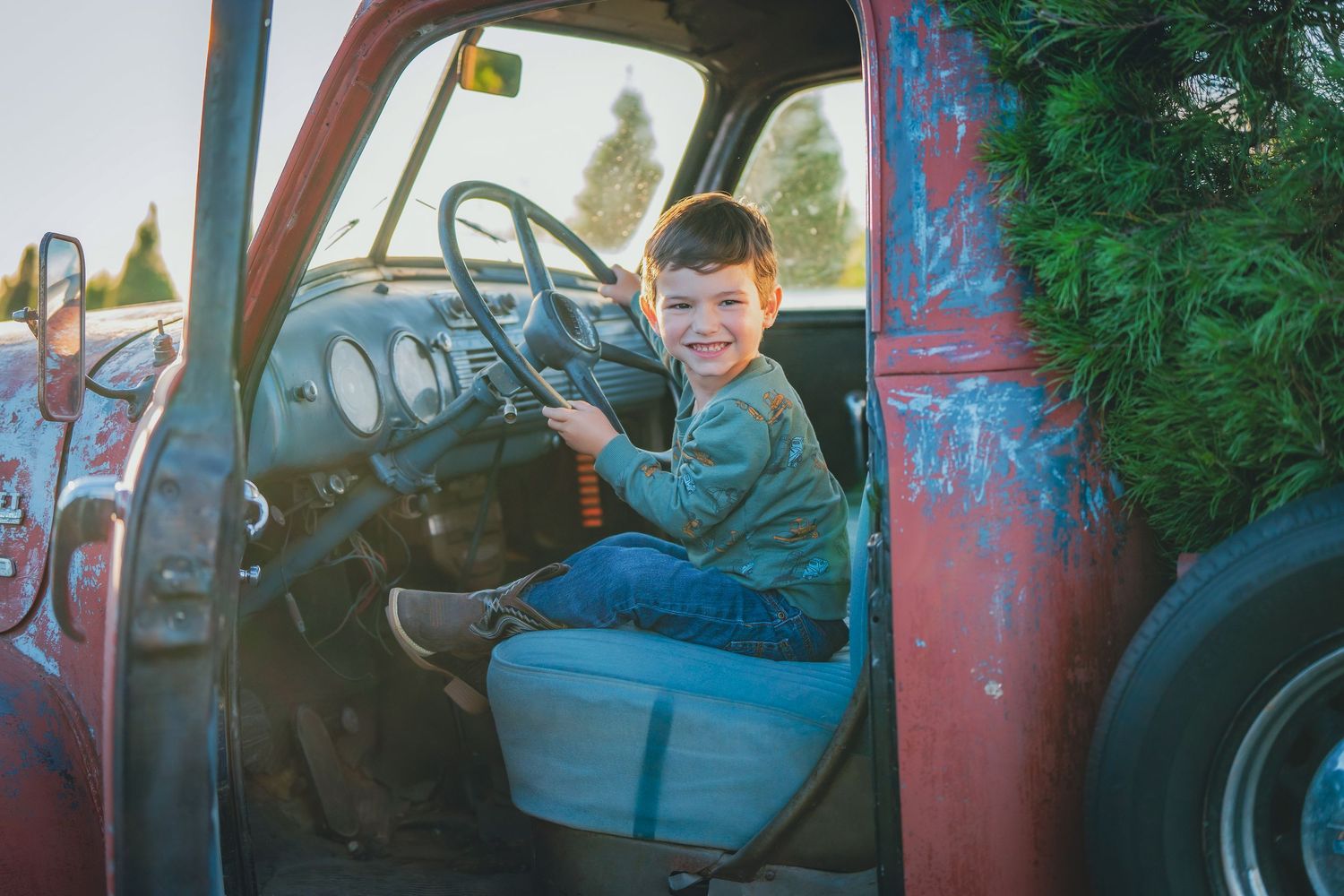 Child sitting in vintage red truck during outdoor photo session.