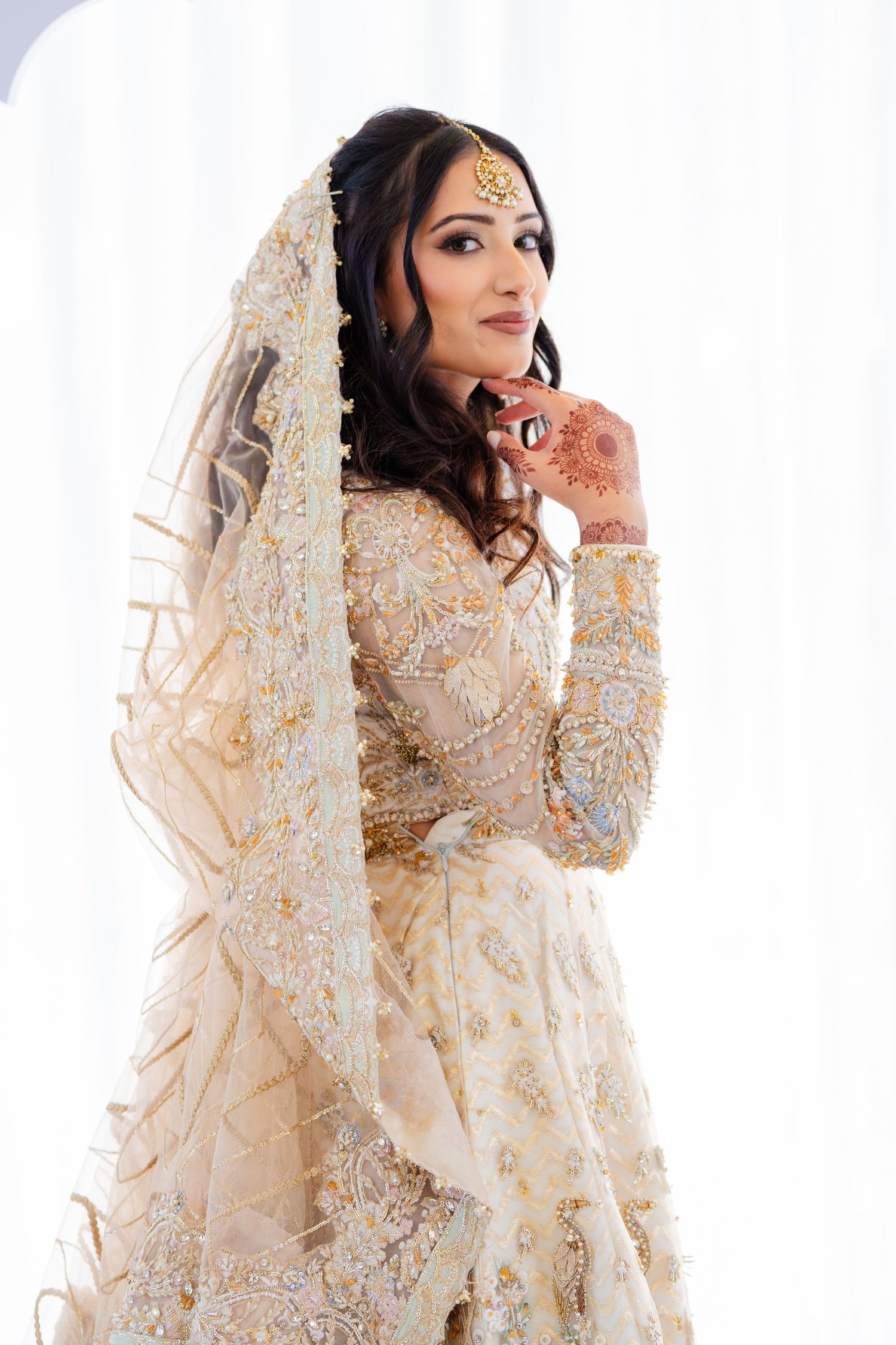 Traditional South Asian bride wearing an ornate cream-colored lehenga with intricate embroidery and veil.