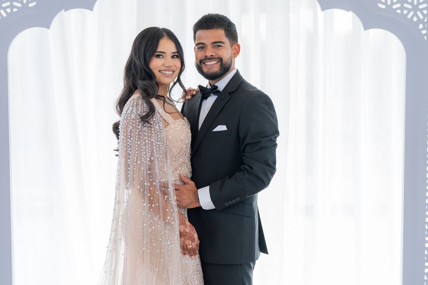 Wedding couple shares a romantic moment against white drapes and elegant decor.