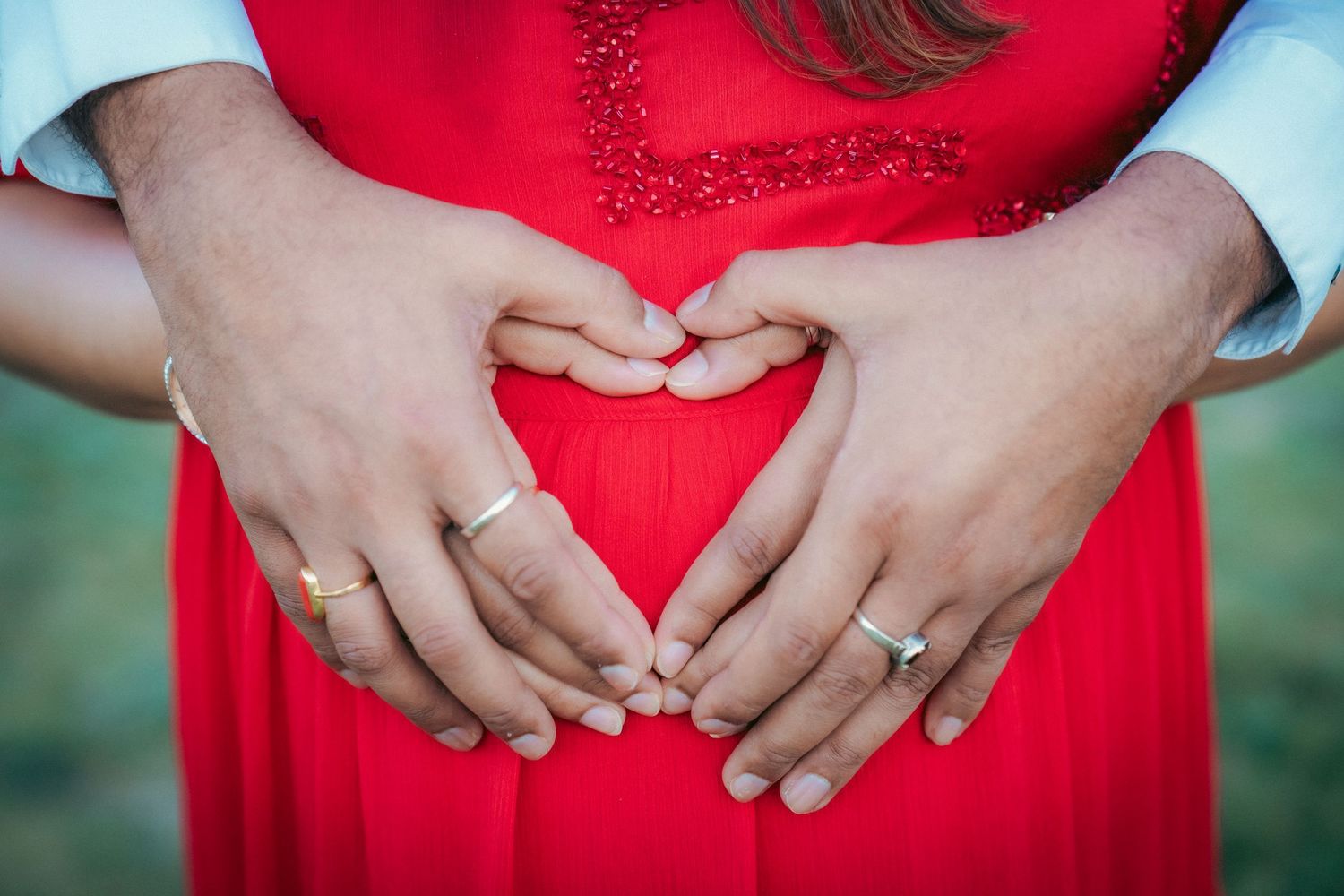 Close-up shots of hands making heart shapes against a red dress.
