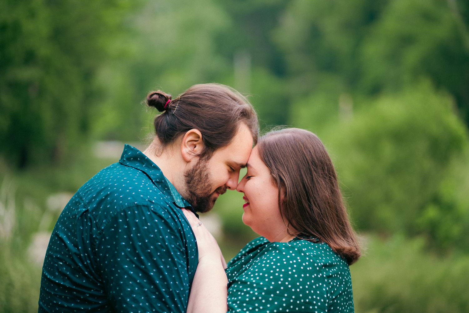 Romantic couple in green attire sharing intimate moment in lush garden setting.
