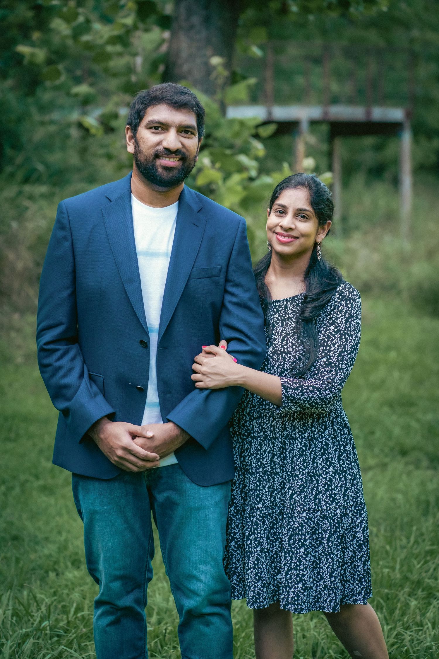 A couple poses together in a garden setting wearing coordinated blue outfits.