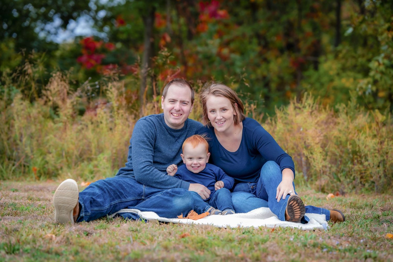 A family in coordinating blue outfits sitting on a white blanket during an autumn photo session.