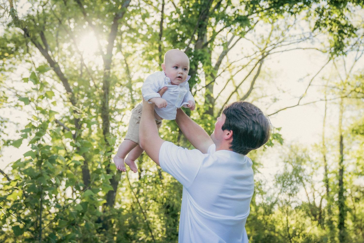 Joyful outdoor family photoshoot with natural sunlight filtering through trees.