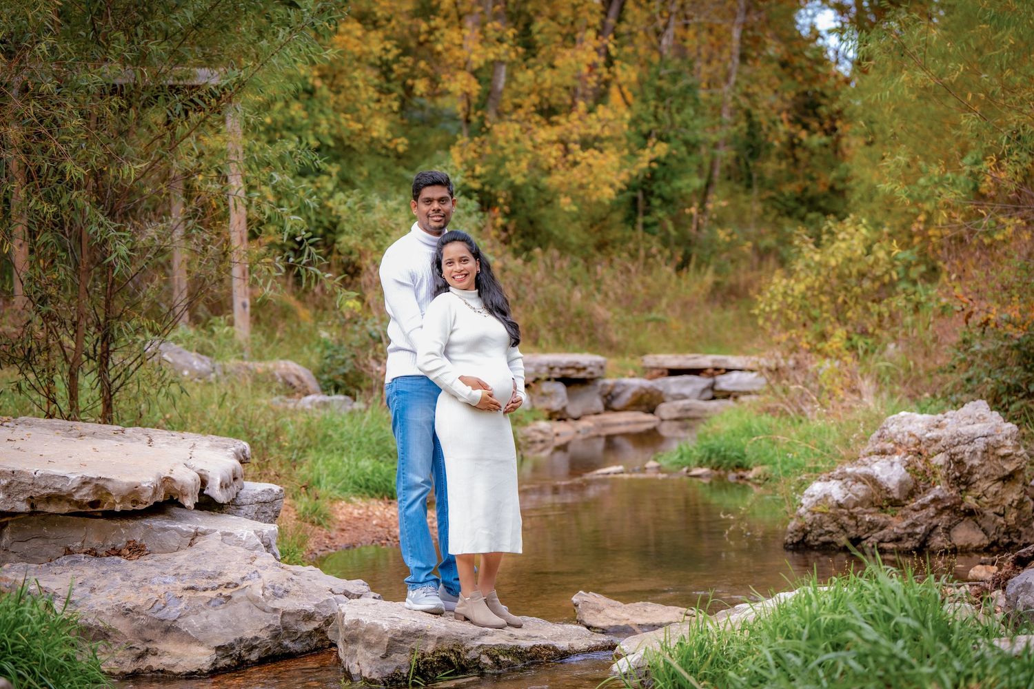 Couple standing on rocks by a stream during autumn with fall foliage in background.