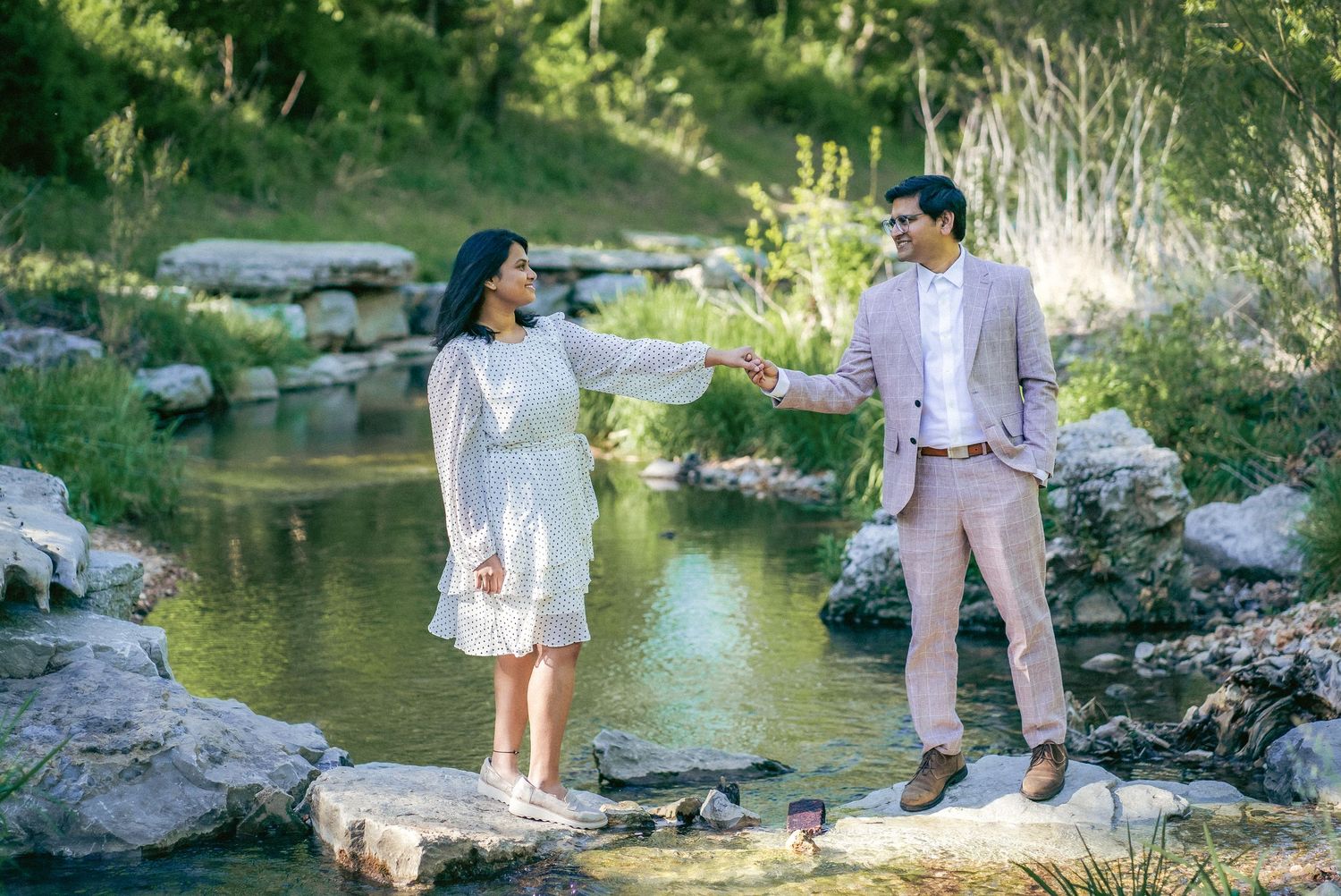 A couple poses playfully near a scenic stream with rocks and greenery in the background.