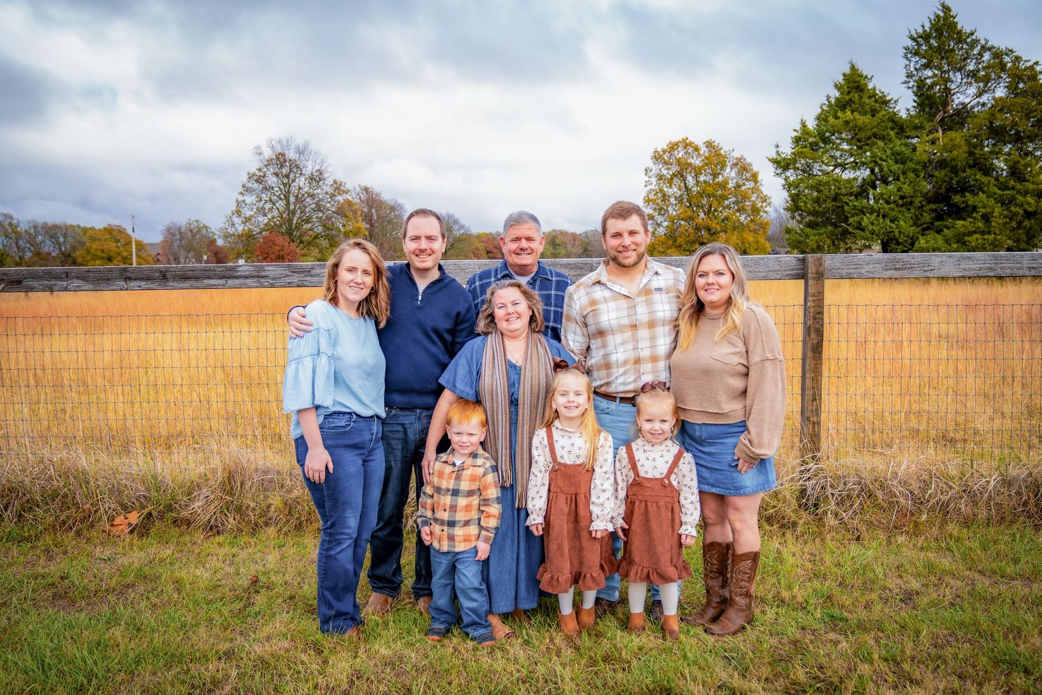 Group portrait of family members lined up against a rustic wooden fence in a field.