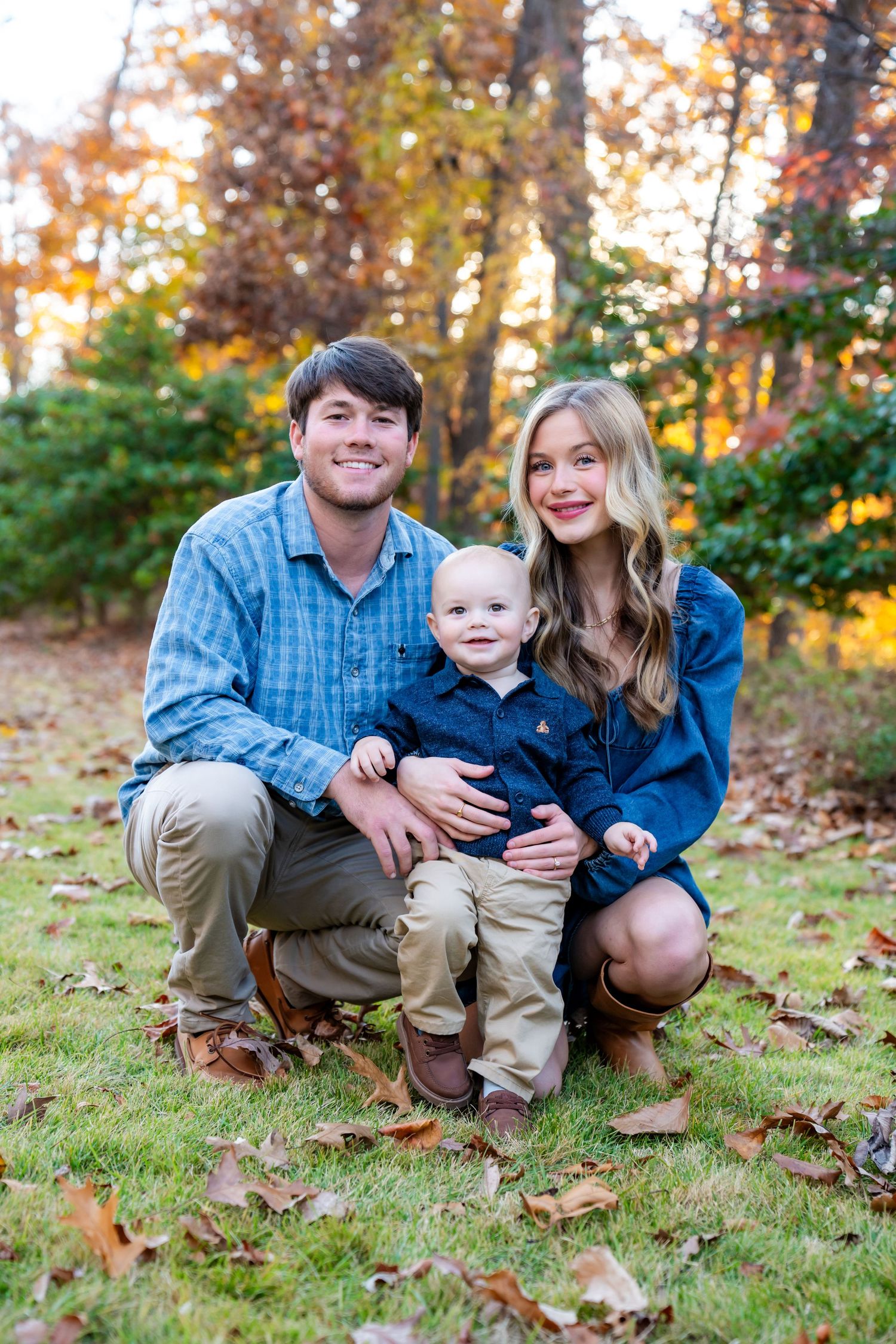 Family sitting together on grass with fall leaves in outdoor setting.