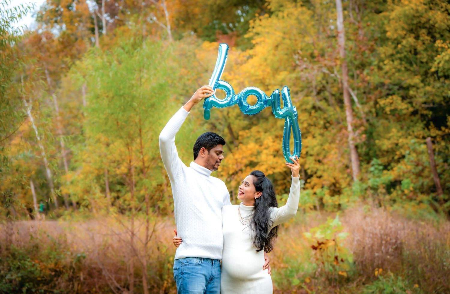 A couple celebrates with joyful poses against a backdrop of golden autumn trees.